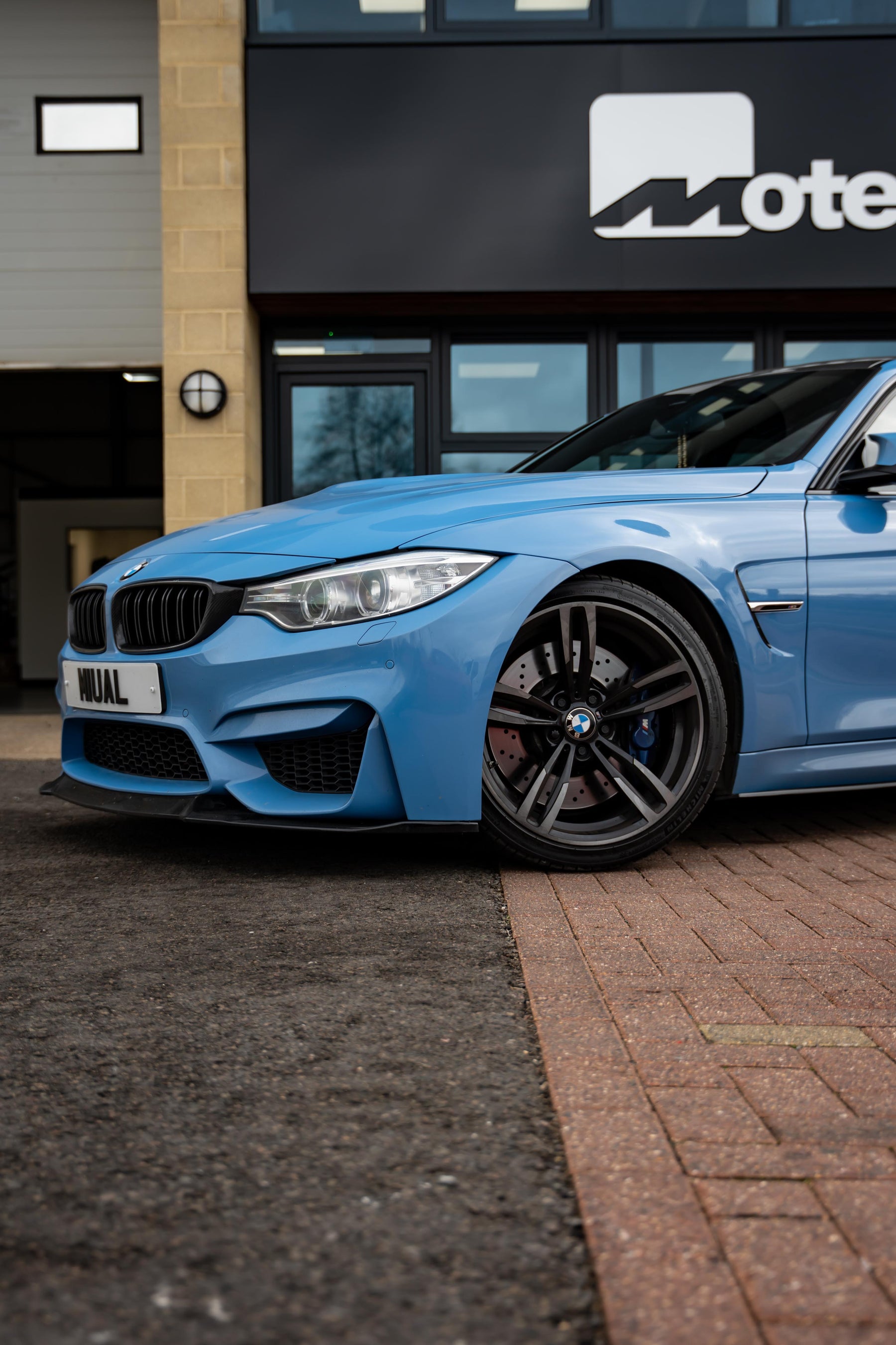Front of a blue BMW outside a building with red bricks on the drive.