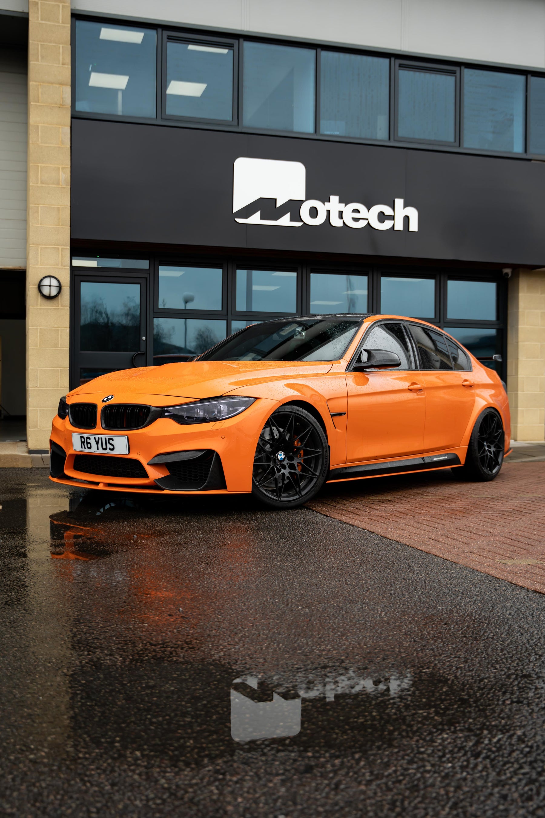 Orange BMW car parked in front of a building with 'Motech' branding.