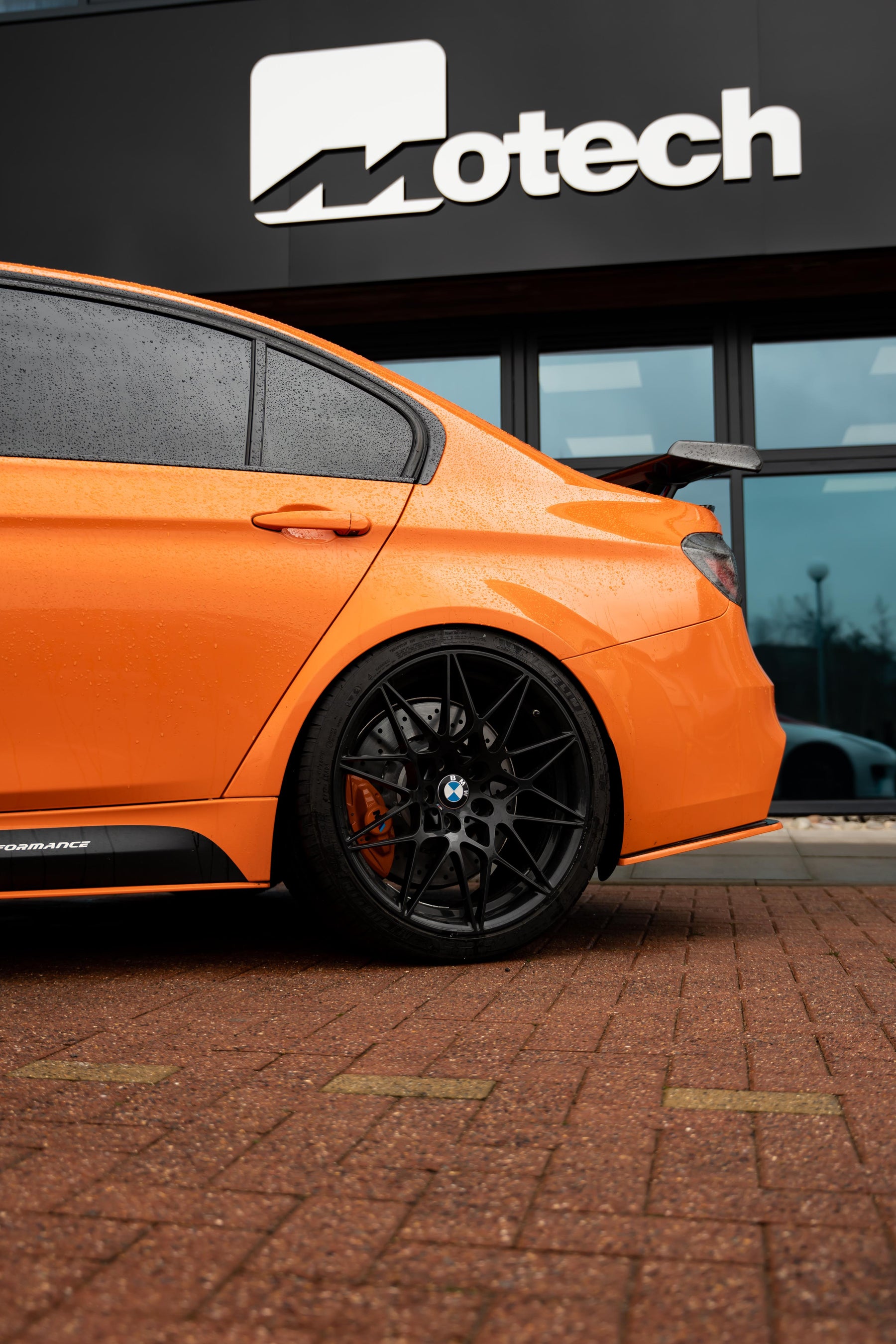 Orange car parked in front of a building with 'Motech' branding.