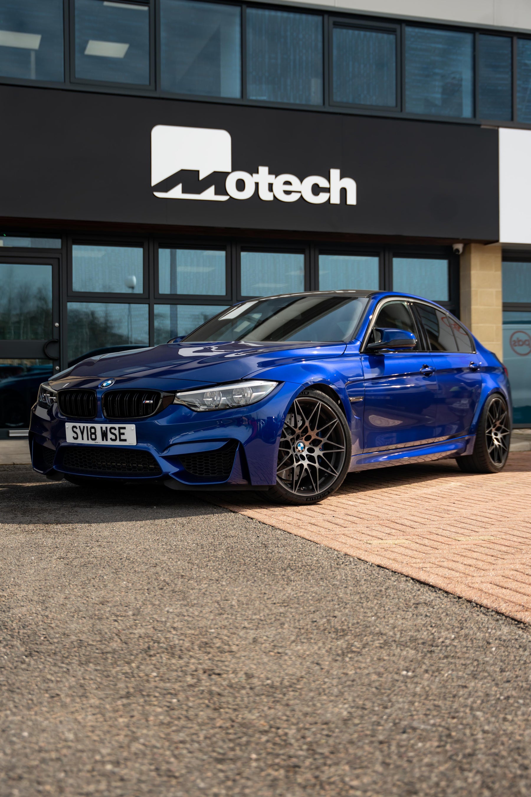 Blue BMW car parked in front of a building with 'Motech' branding.