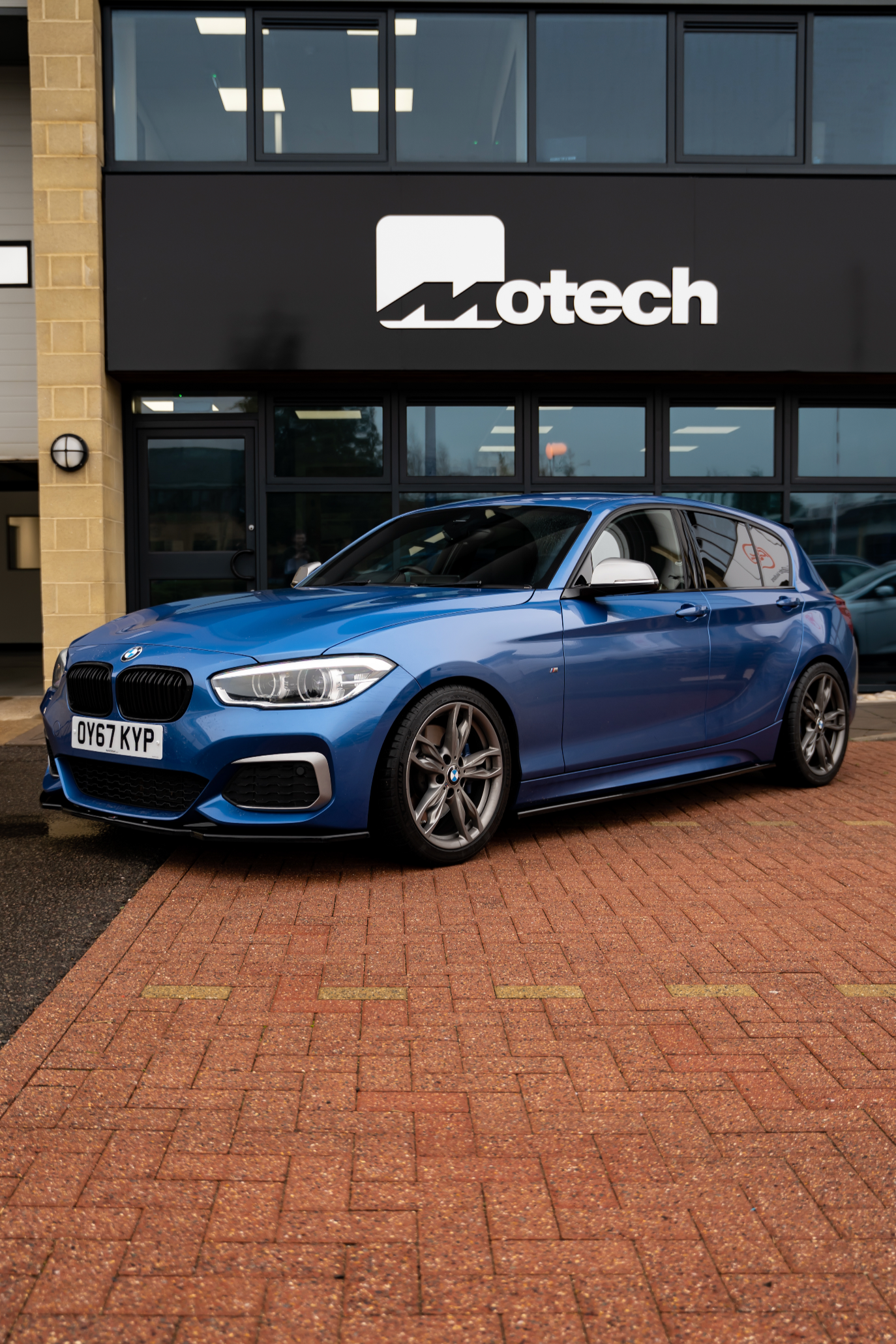 Blue BMW car on Motech stance springs parked in front of a building with 'Motech' branding.