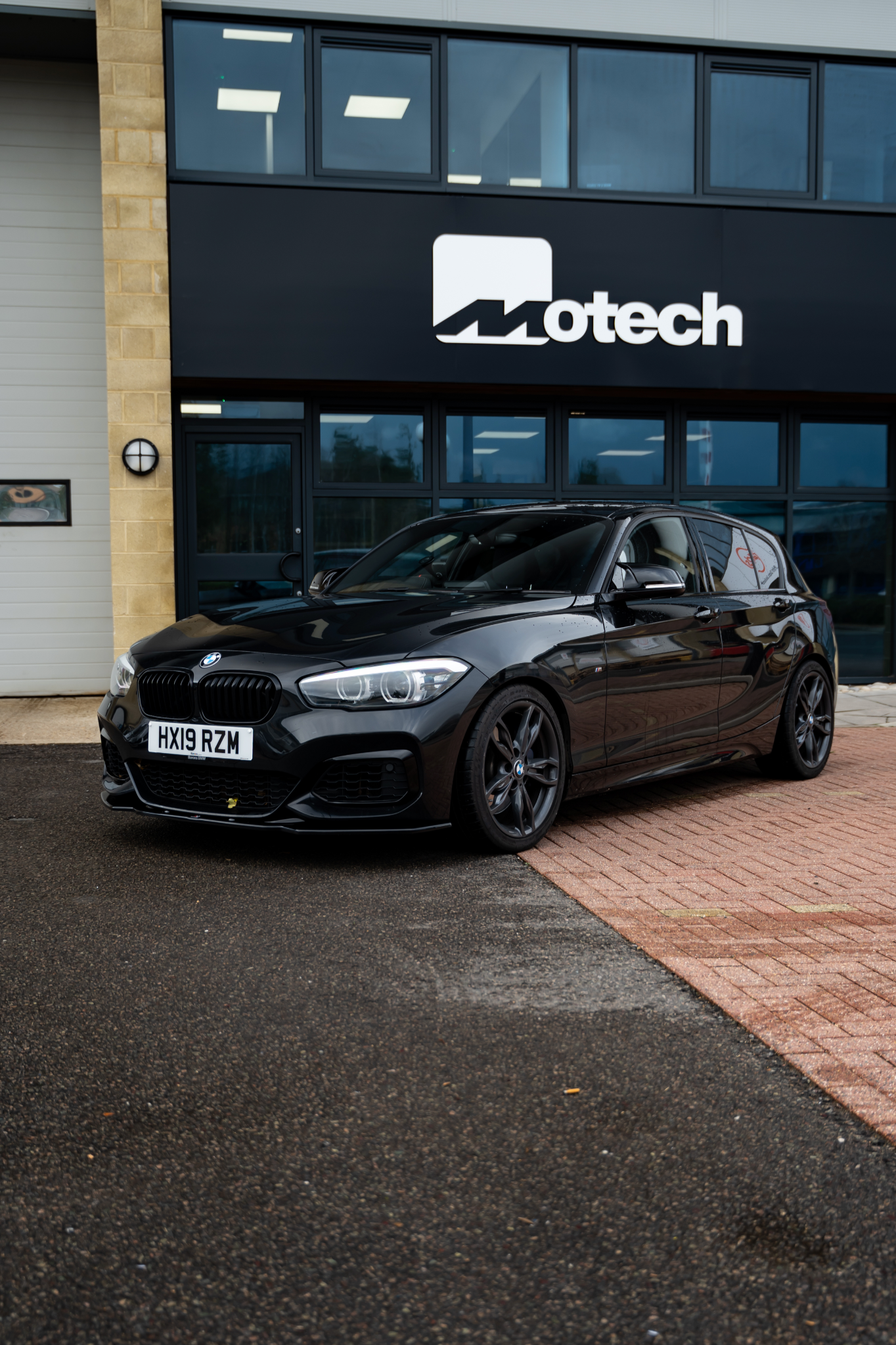 Black BMW with Motech stance springs parked in front of a building with a Motech logo.