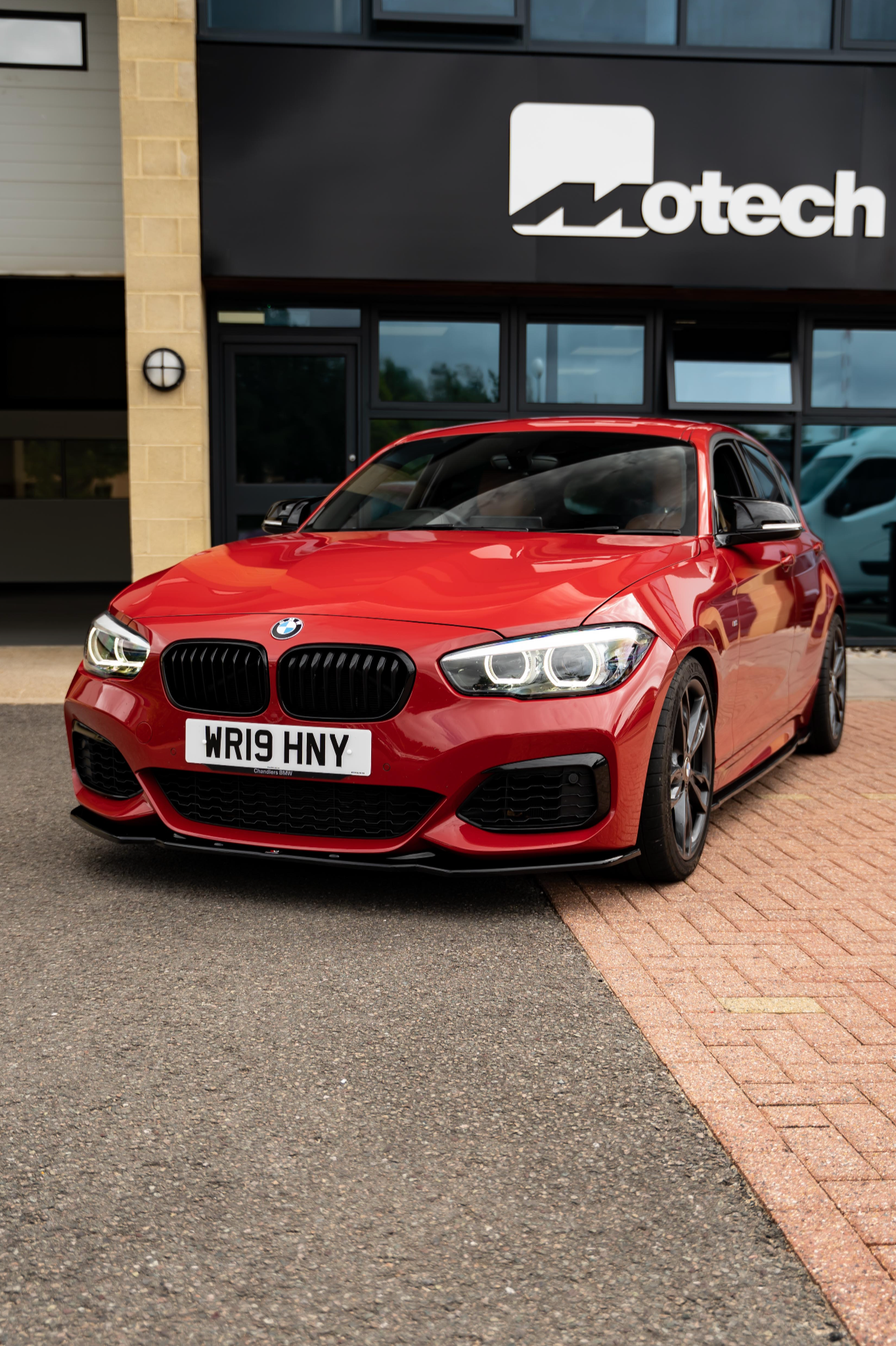 Red BMW car on Motech Stance springs parked in front of a Motech building