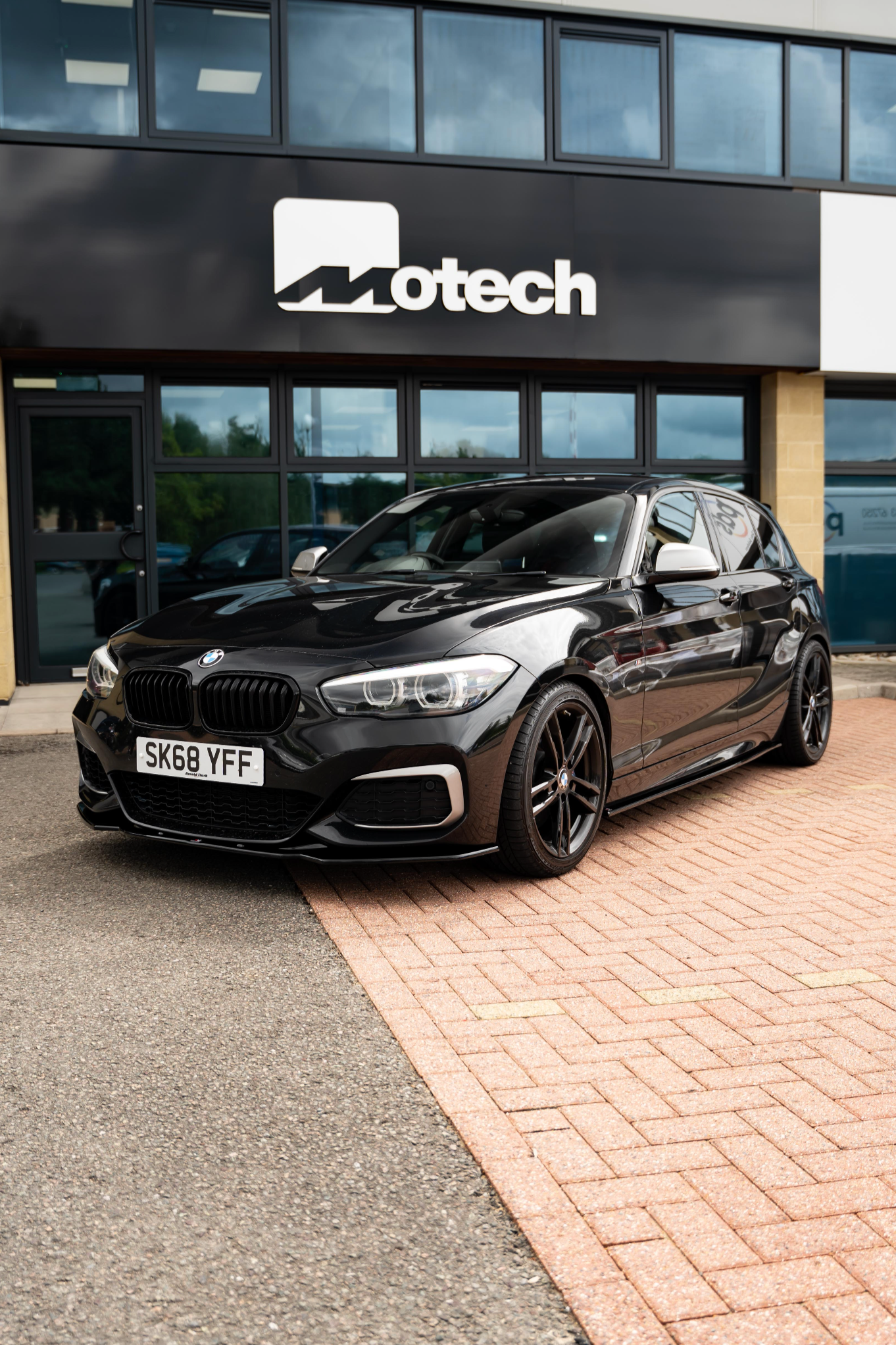 Black BMW car parked in front of a building with 'Motech' branding.