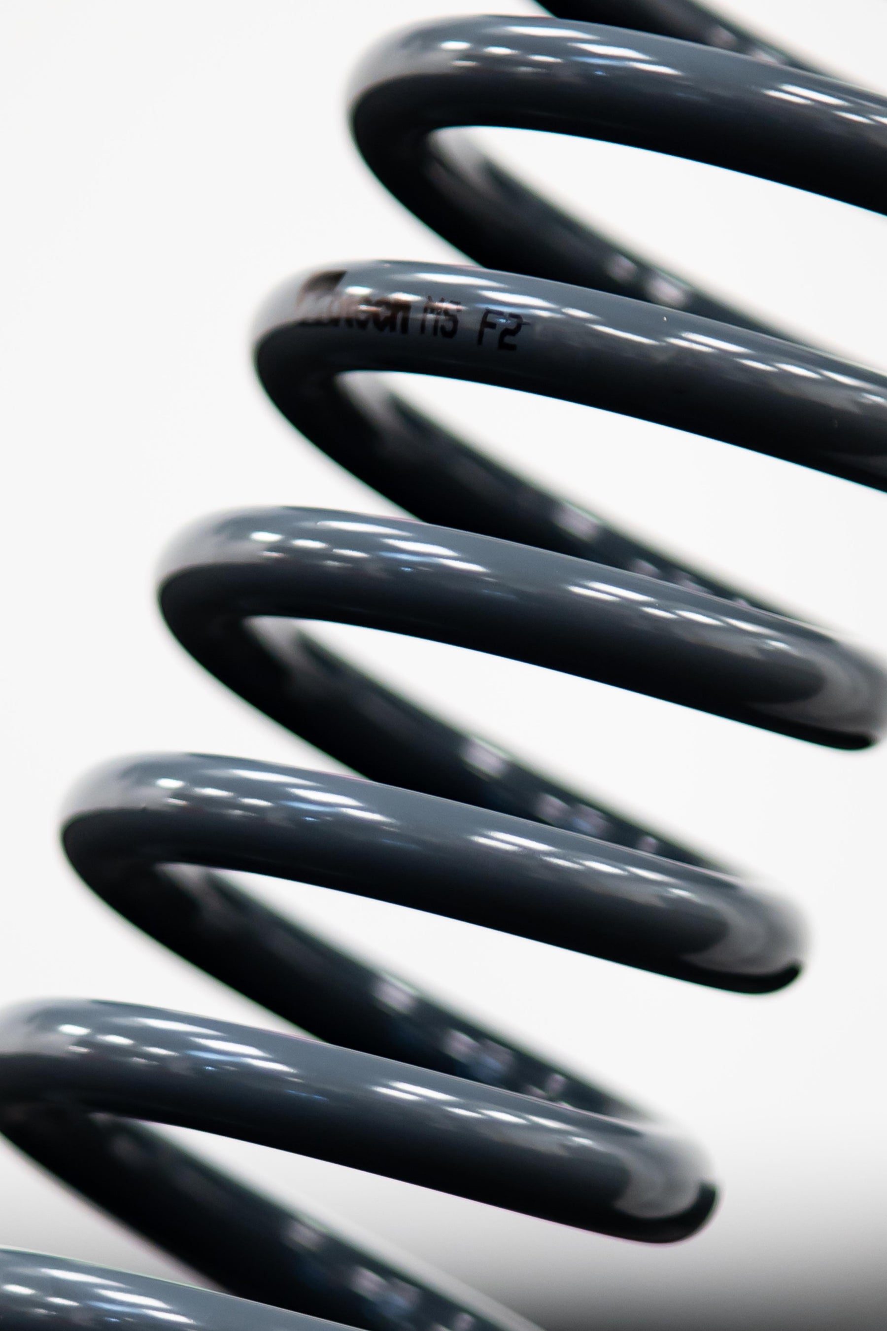 A close-up image of a black coil spring, which is part of the Motech Stance + suspension kit.