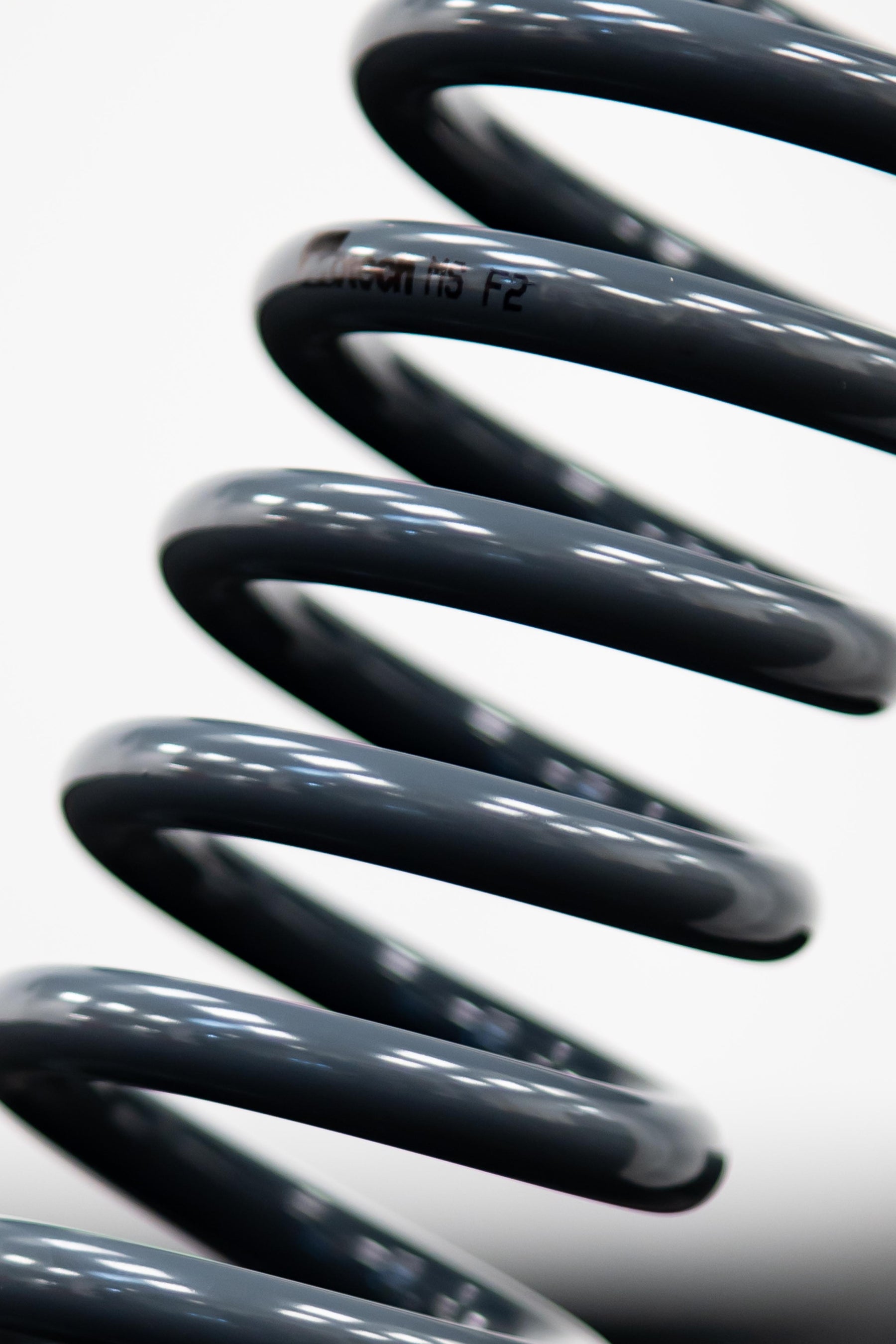 A close-up of a black Motech stance lowering spring, showing its surface and the brand name 'Motech' visible on the spring.