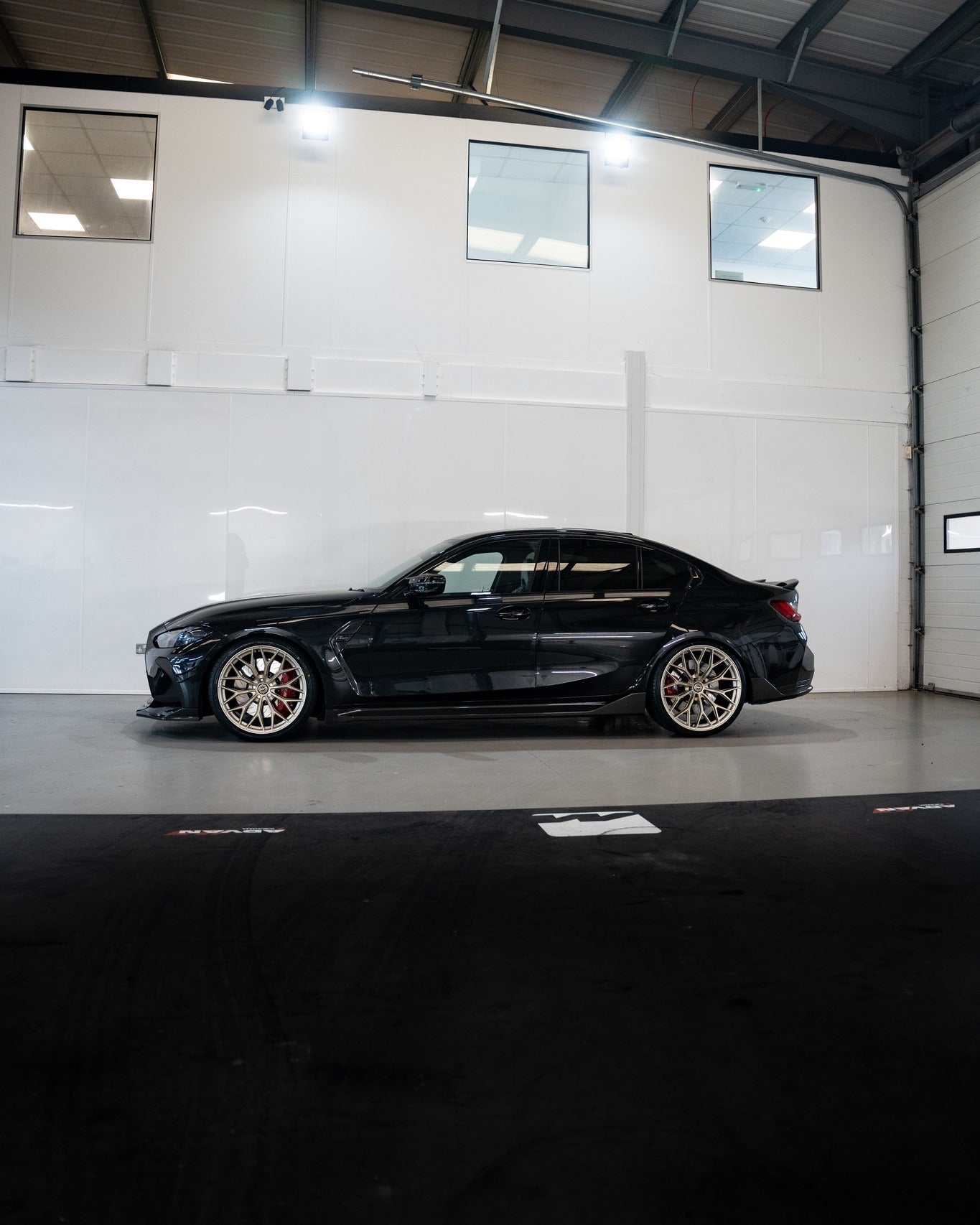 Side-on shot of an M3 G80 with Frozen Gold M-WX's and on Motech Stance springs in a car workshop. 