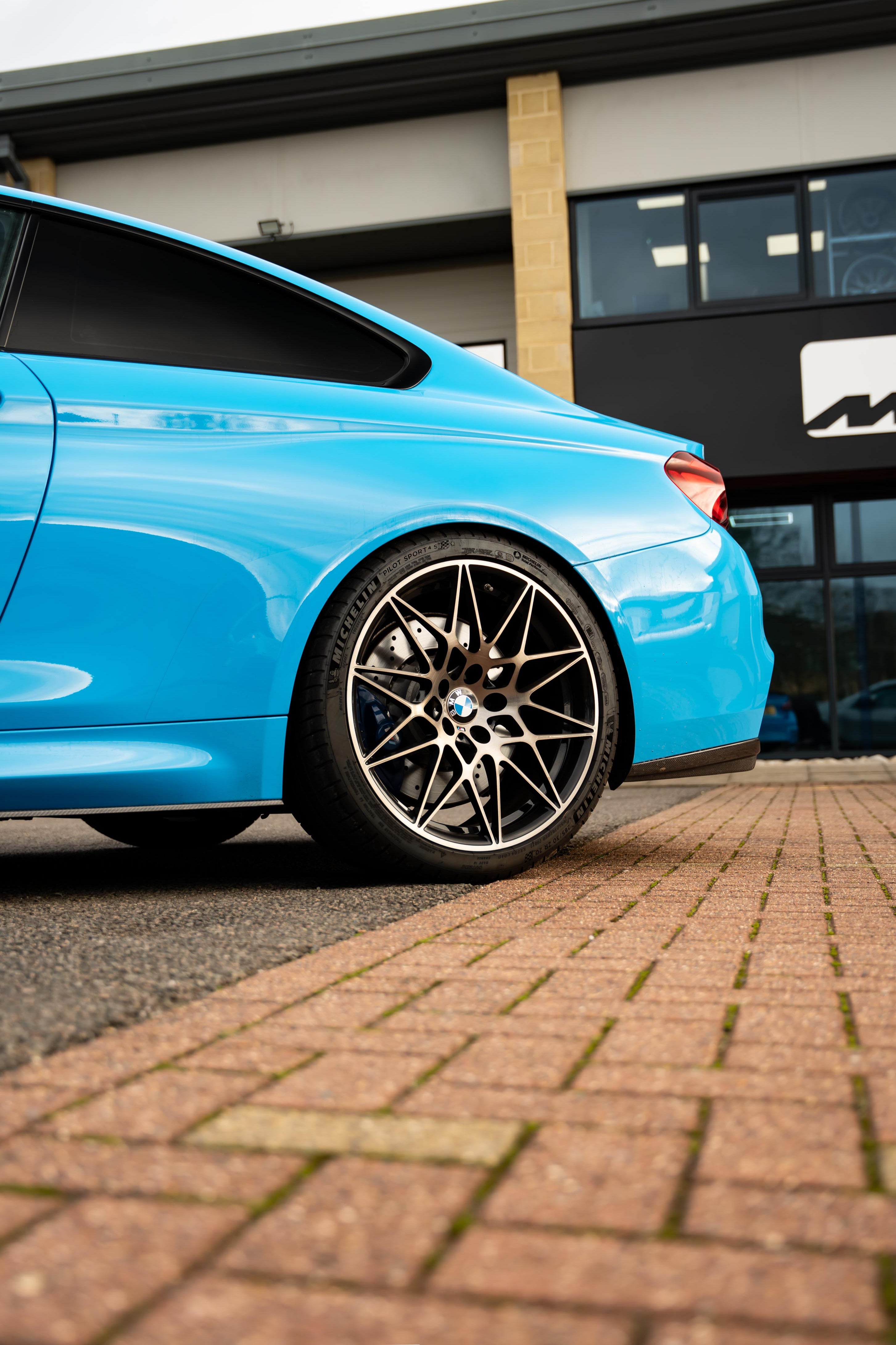 Blue BMW with black rims on a brick road in front of a building. Car is on Motech Stance Springs