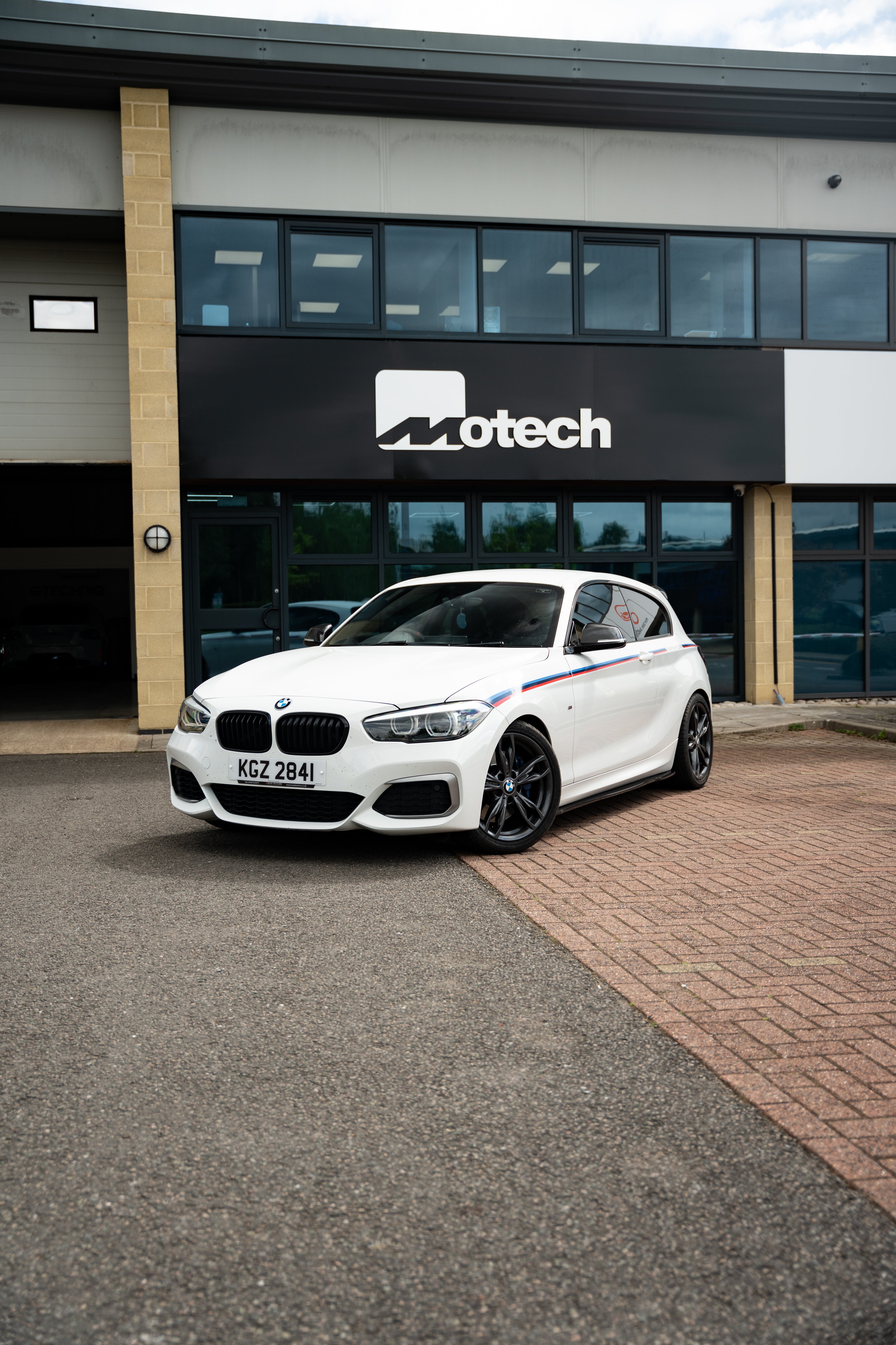 White BMW car parked in front of a building with the Motech logo.