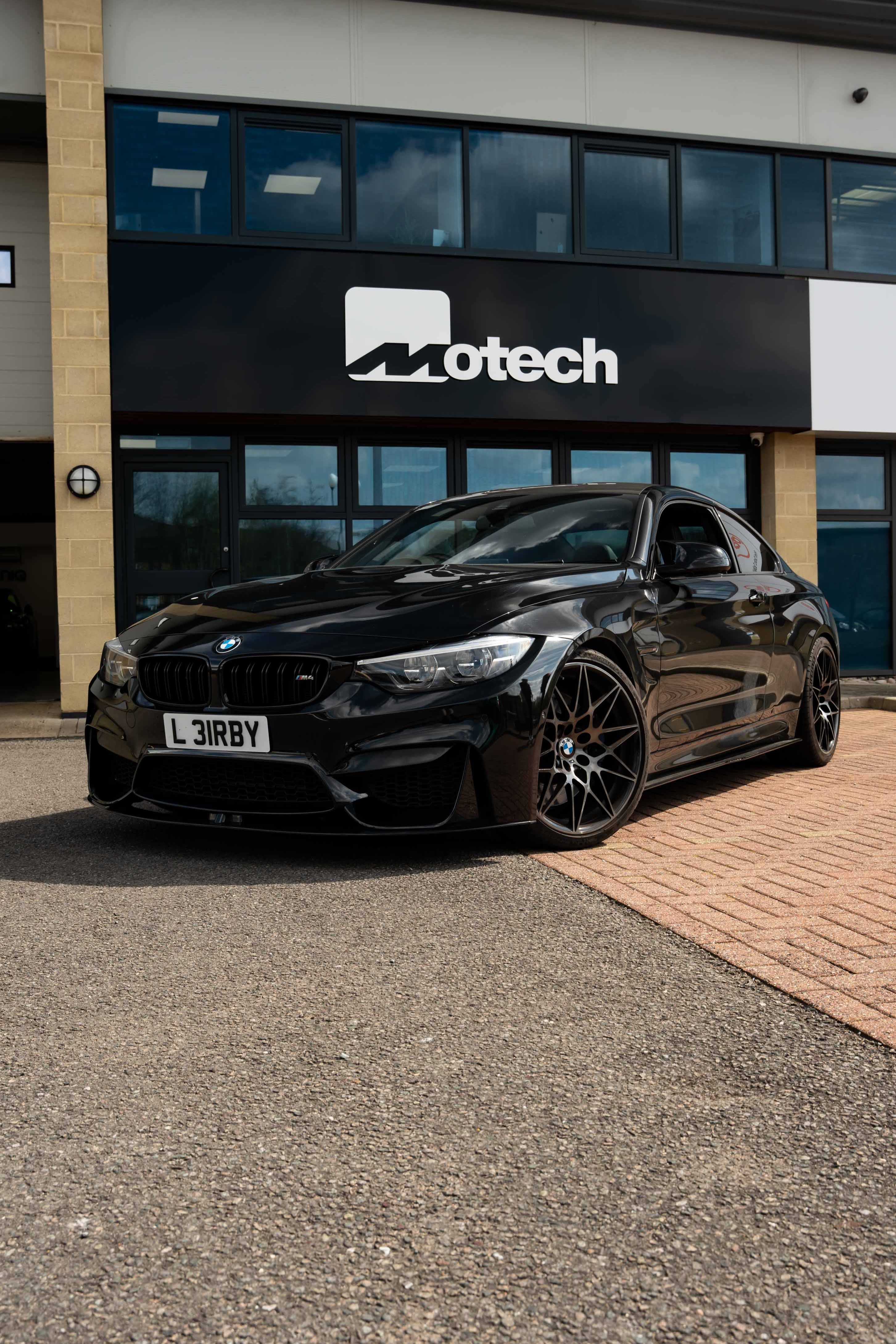 Black BMW car on Motech Stance Springs parked in front of a building with 'Motech' branding.
