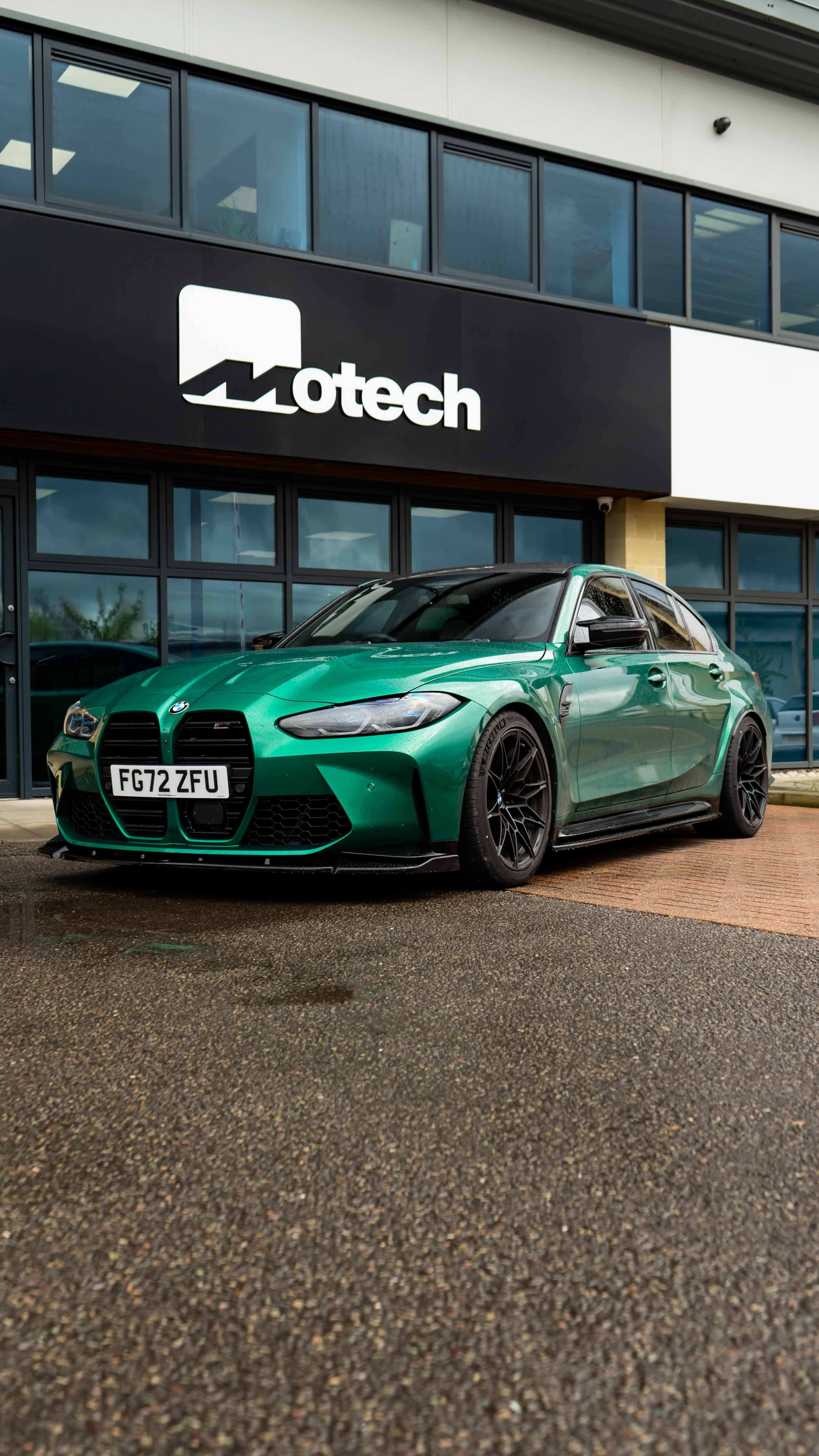Green BMW M3 G80 on Motech Stance springs parked outside a building with 'Motech' branding. 