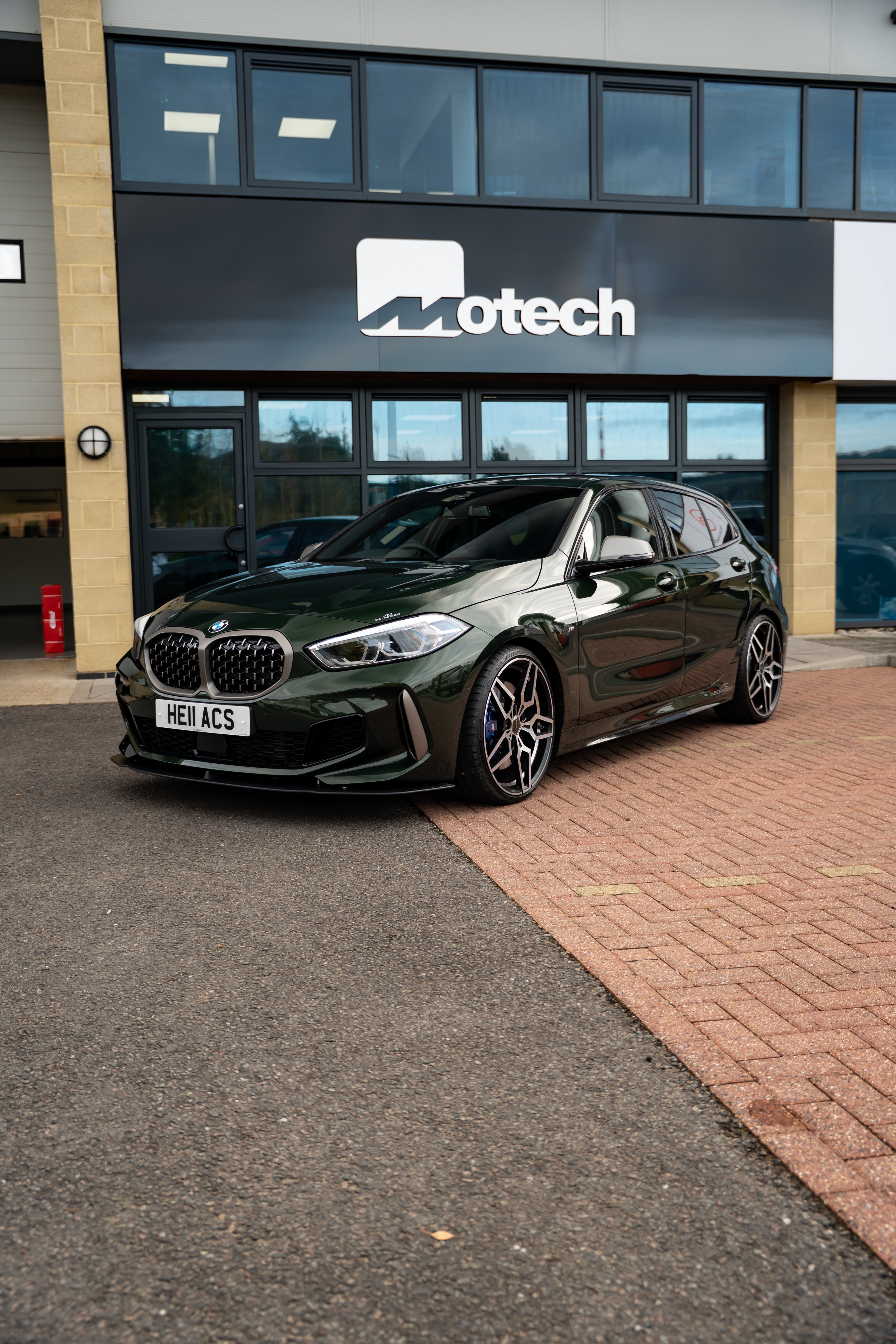 Green BMW car with an AC Schnitzer Front Splitter parked in front of a building with 'Motech' branding.