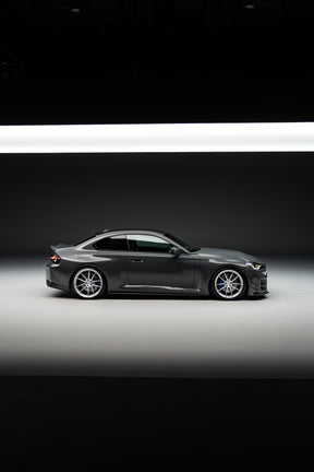 Side-on shot of a BMW M2 G87 with aftermarket wheels and lowered on springs in a high-quality photography studio. 