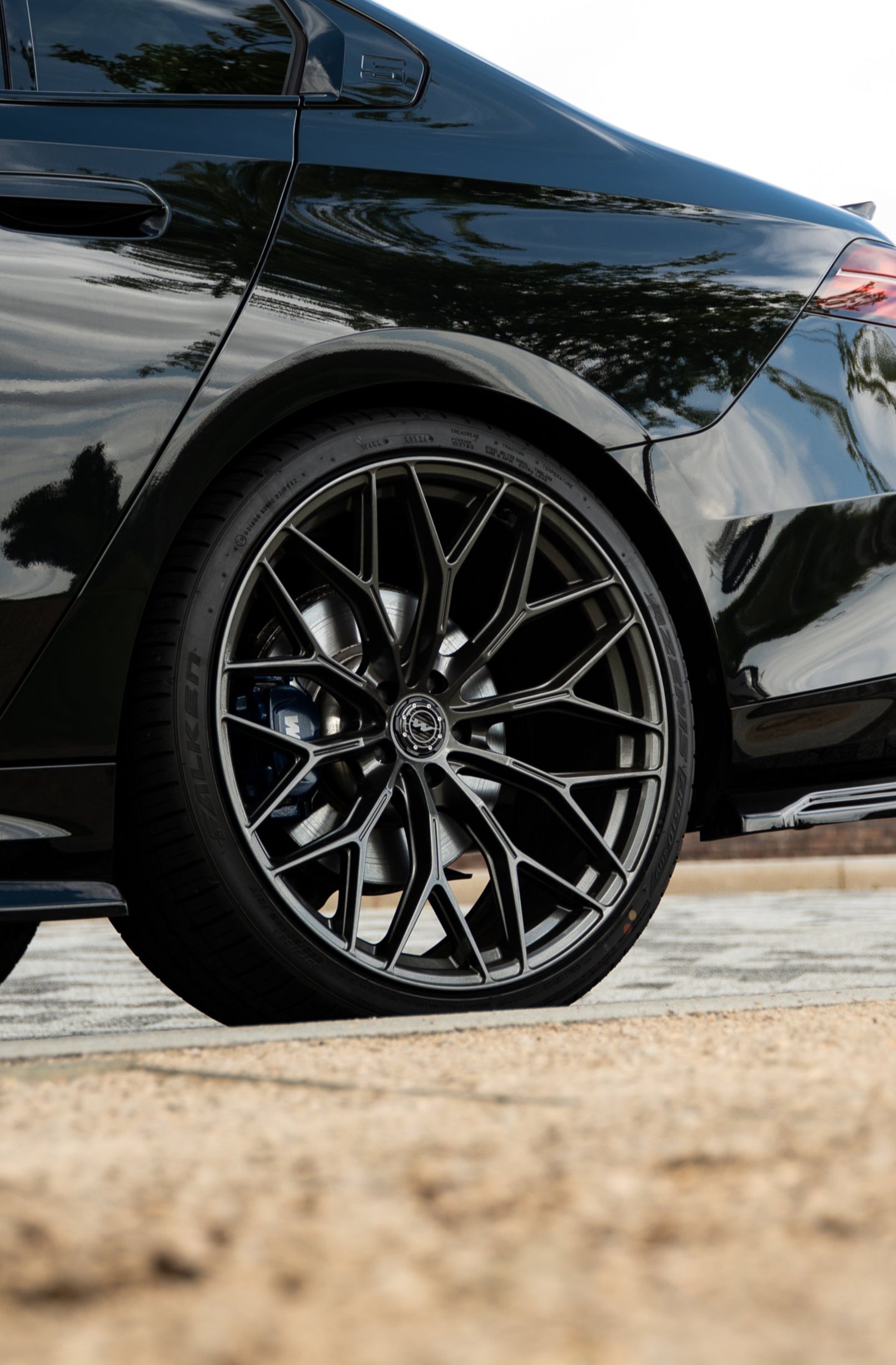 Close-up of a black car's Motech wheel with a detailed 3-piece centre cap on a road.
