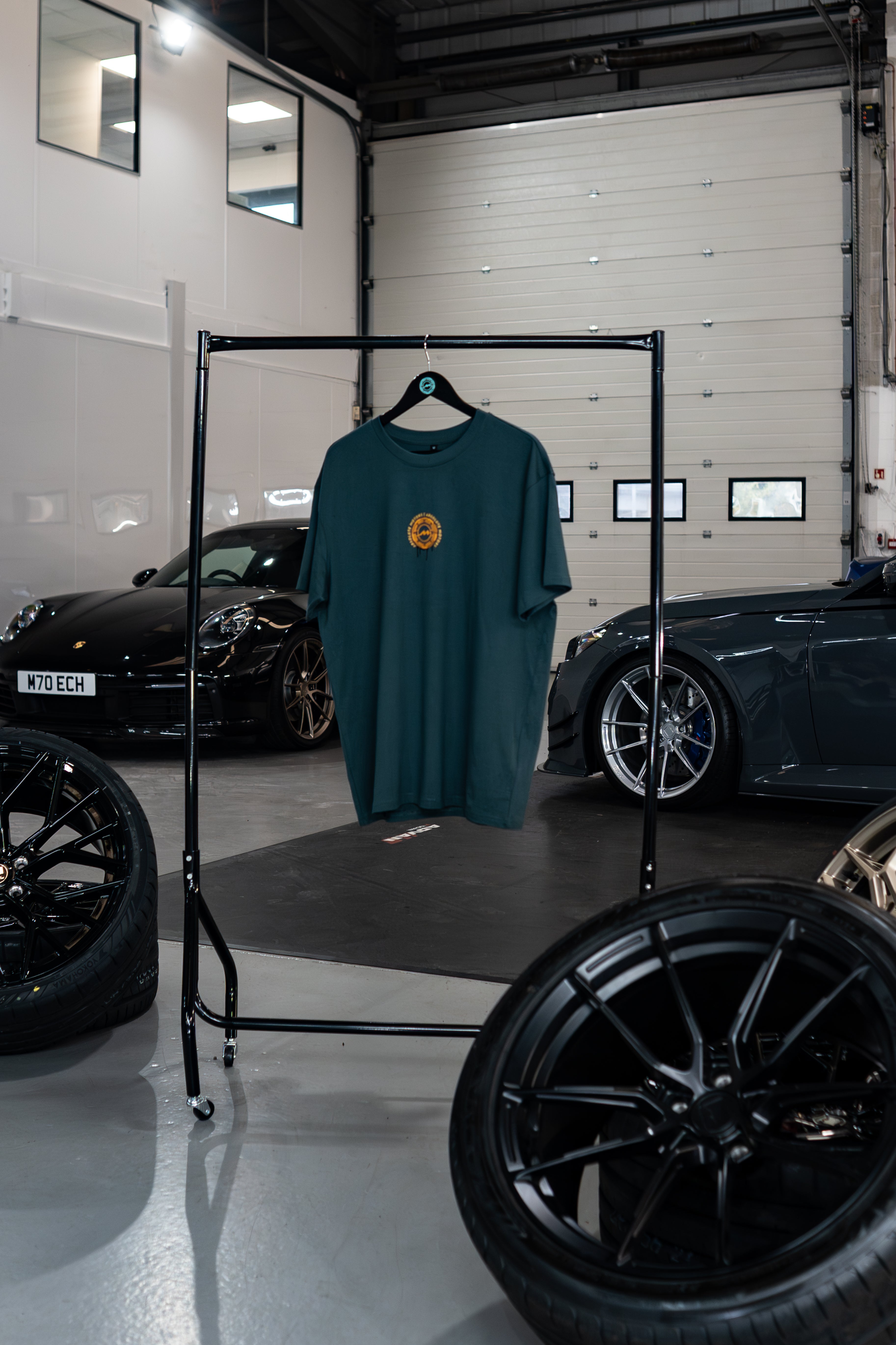 Vantage Collection Buckinghamshire Green Oversized T-shirt on a rack in a garage with cars and tires in the background