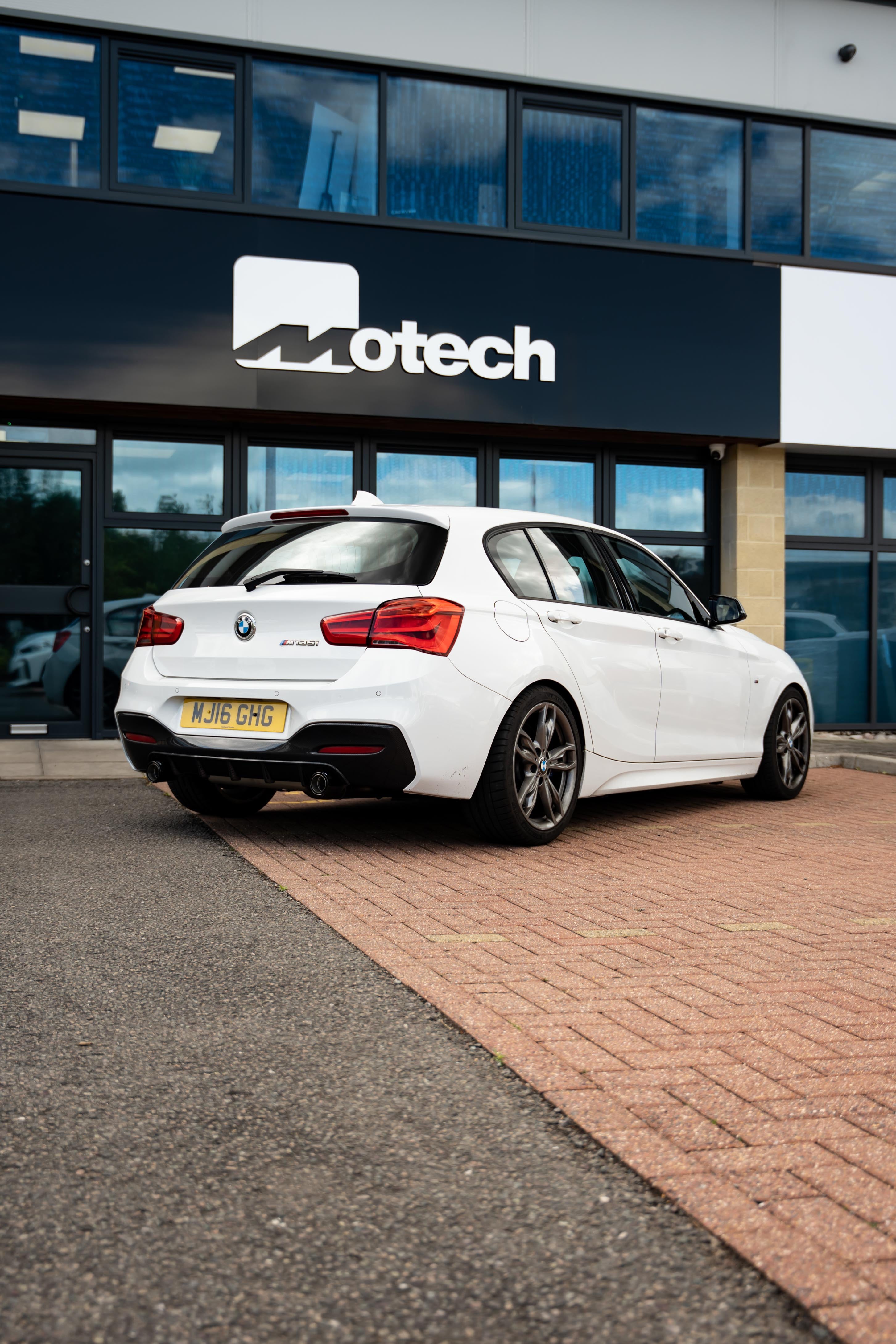 White BMW 1 Series parked outside a building with 'Motech' branding. 