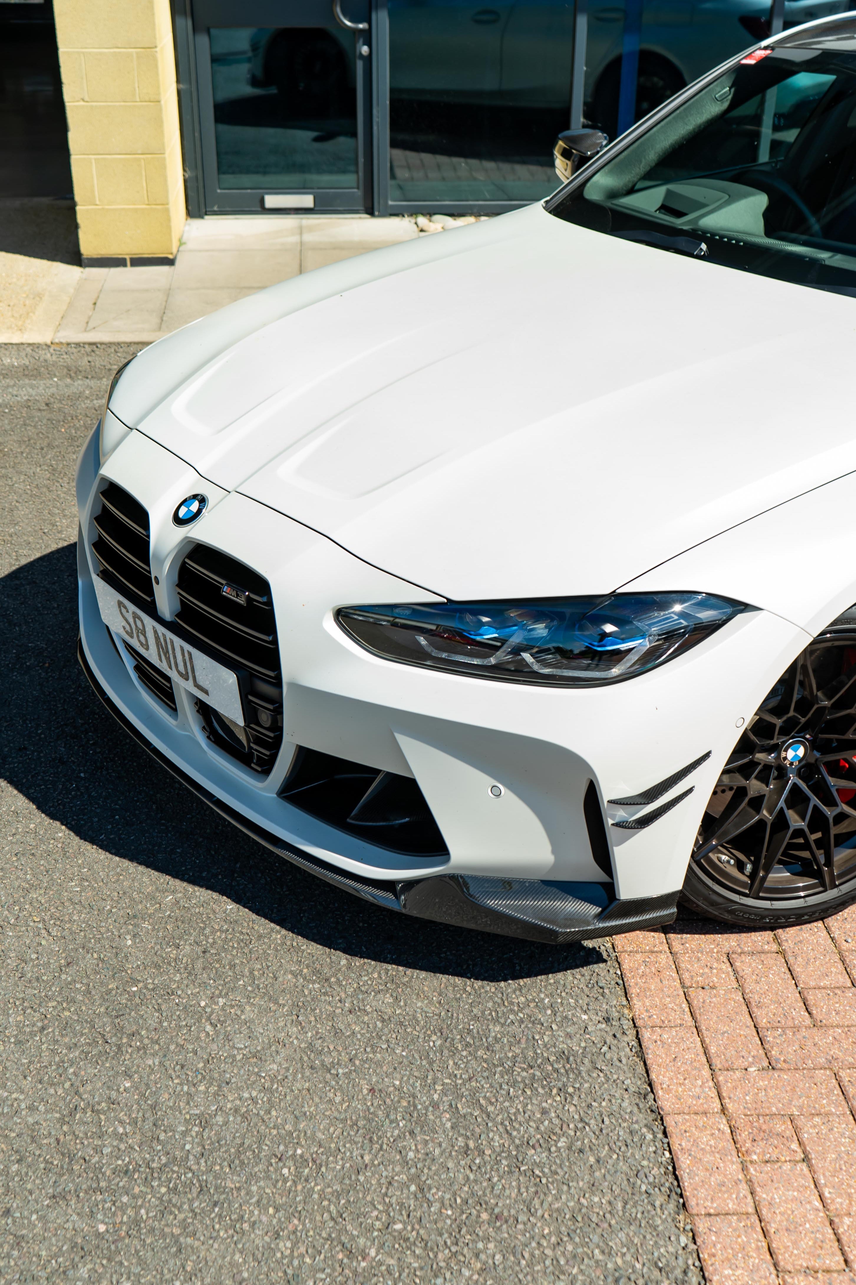 Front of a White BMW M3 with an aftermarket M-Performance Carbon Front Splitter attached.
