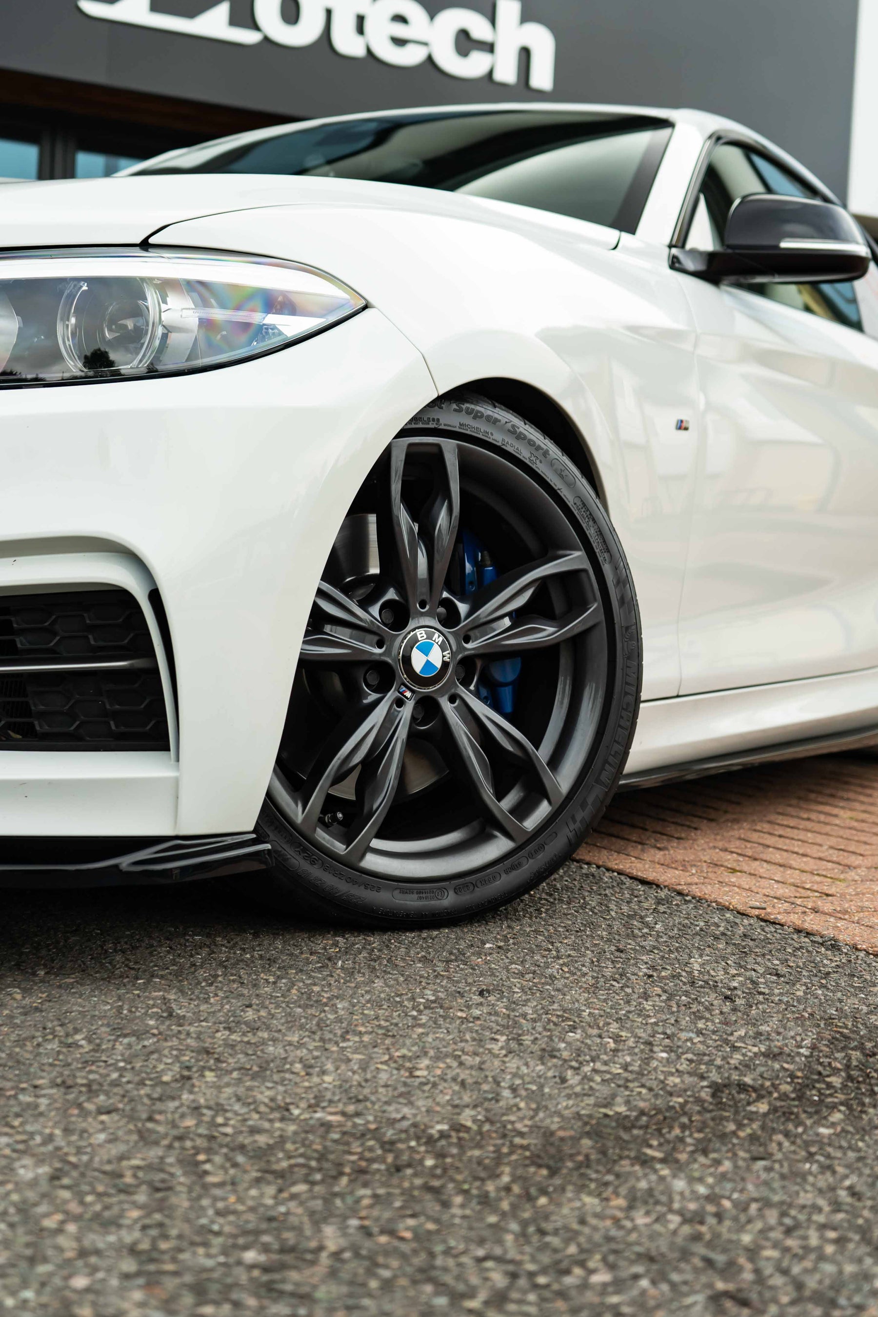 White BMW car on Motech Stance Springs with black rims in front of a Motech branded building.