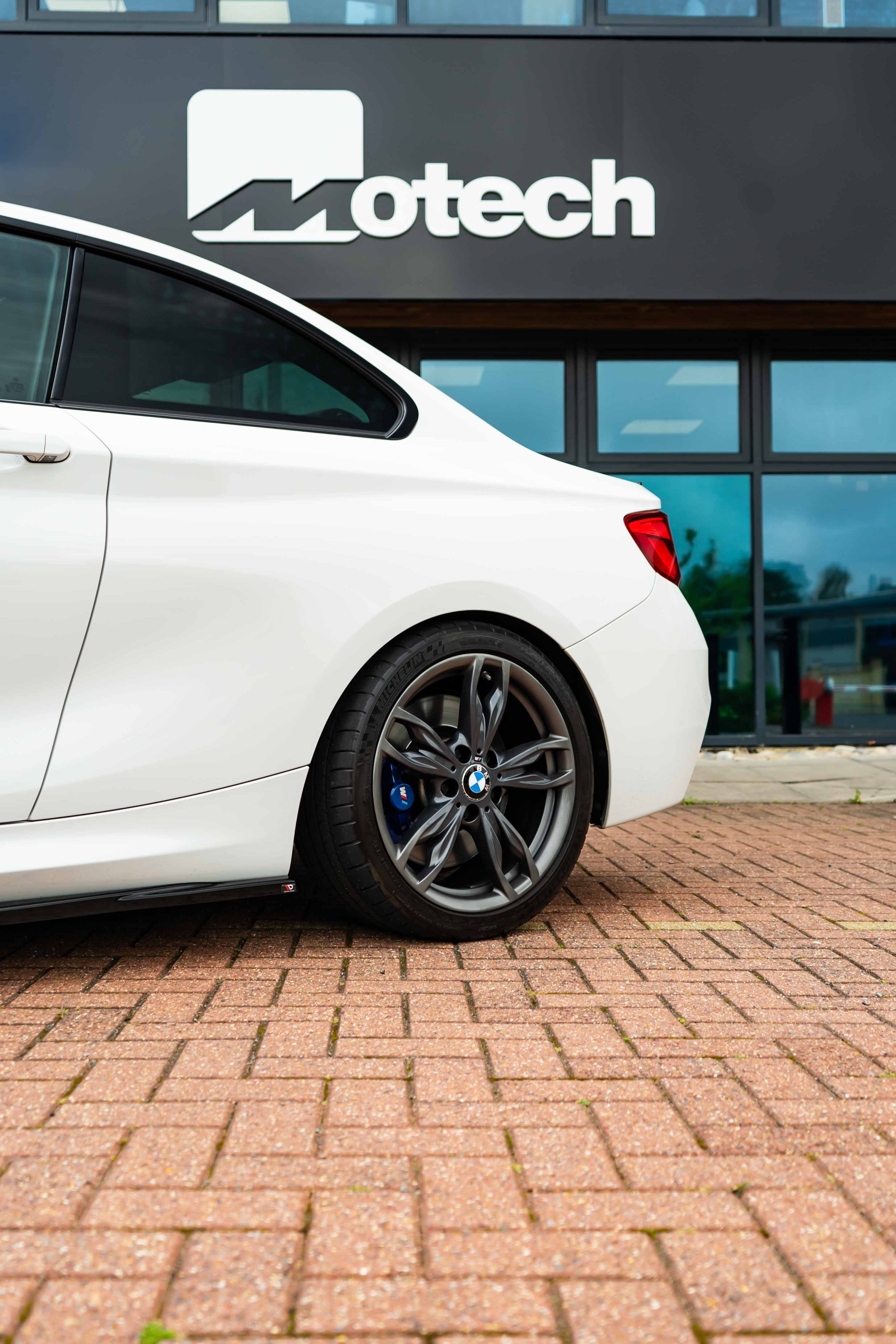 White car on Motech Stance Springs 
parked on a brick pavement in front of a building with 'Motech' branding.