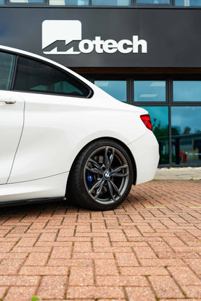 White car on Motech Stance Springs 
parked on a brick pavement in front of a building with 'Motech' branding.