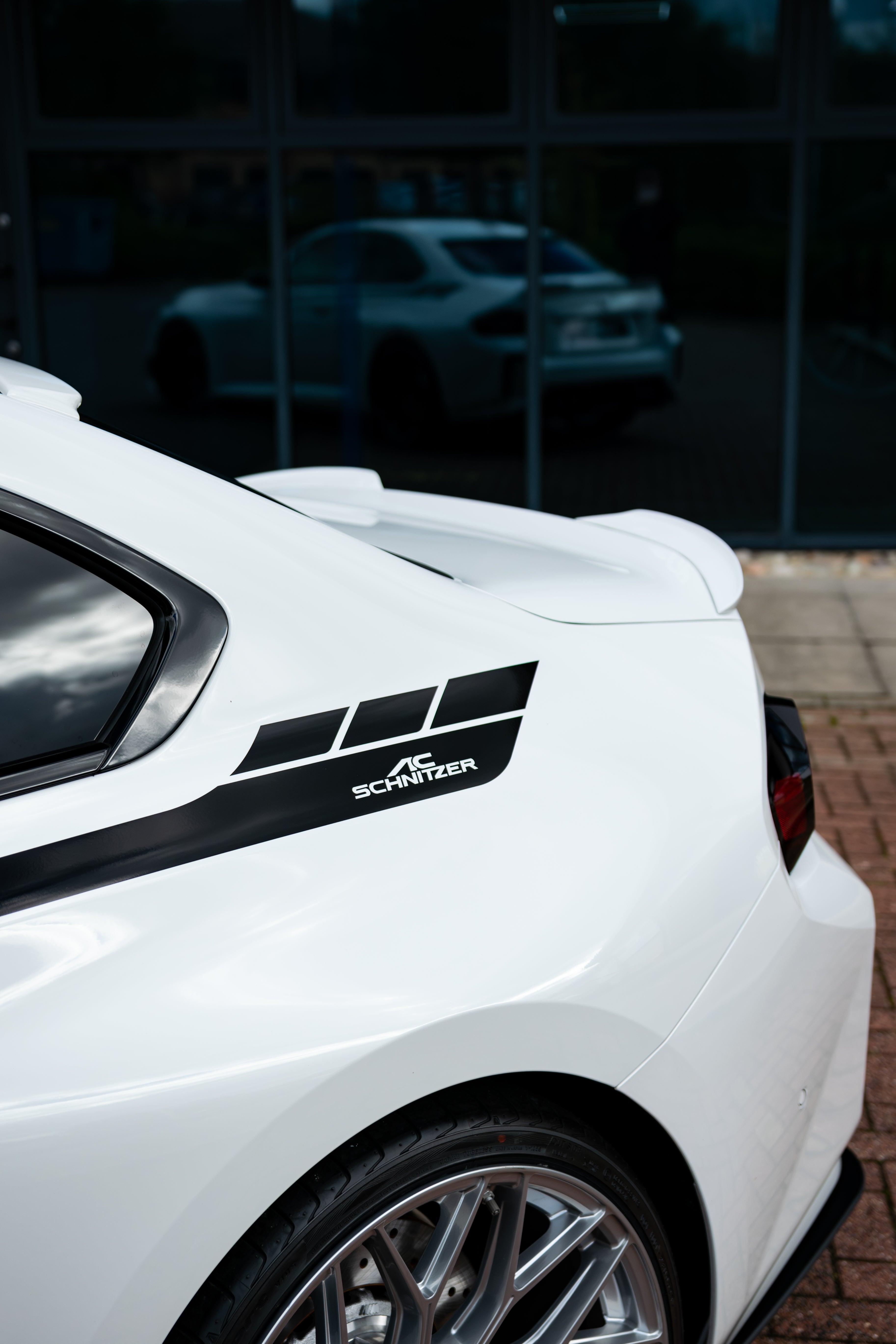 White car with a black decal on the side, parked in front of a glass building.