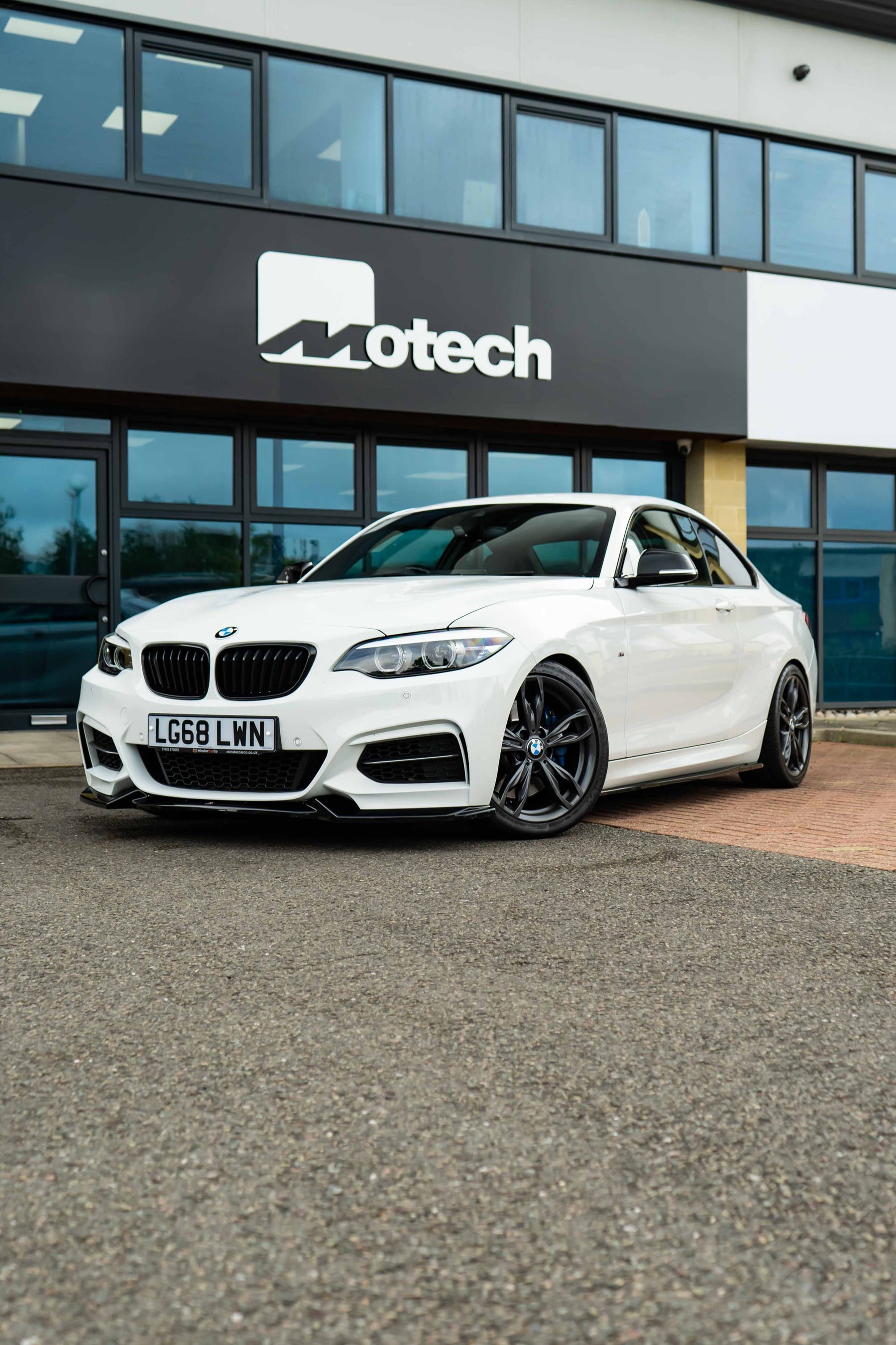 White BMW car on Motech Stance Springs parked in front of a building with 'Motech' branding.