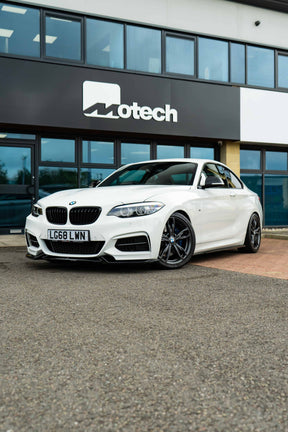 White BMW car on Motech Stance Springs parked in front of a building with 'Motech' branding.