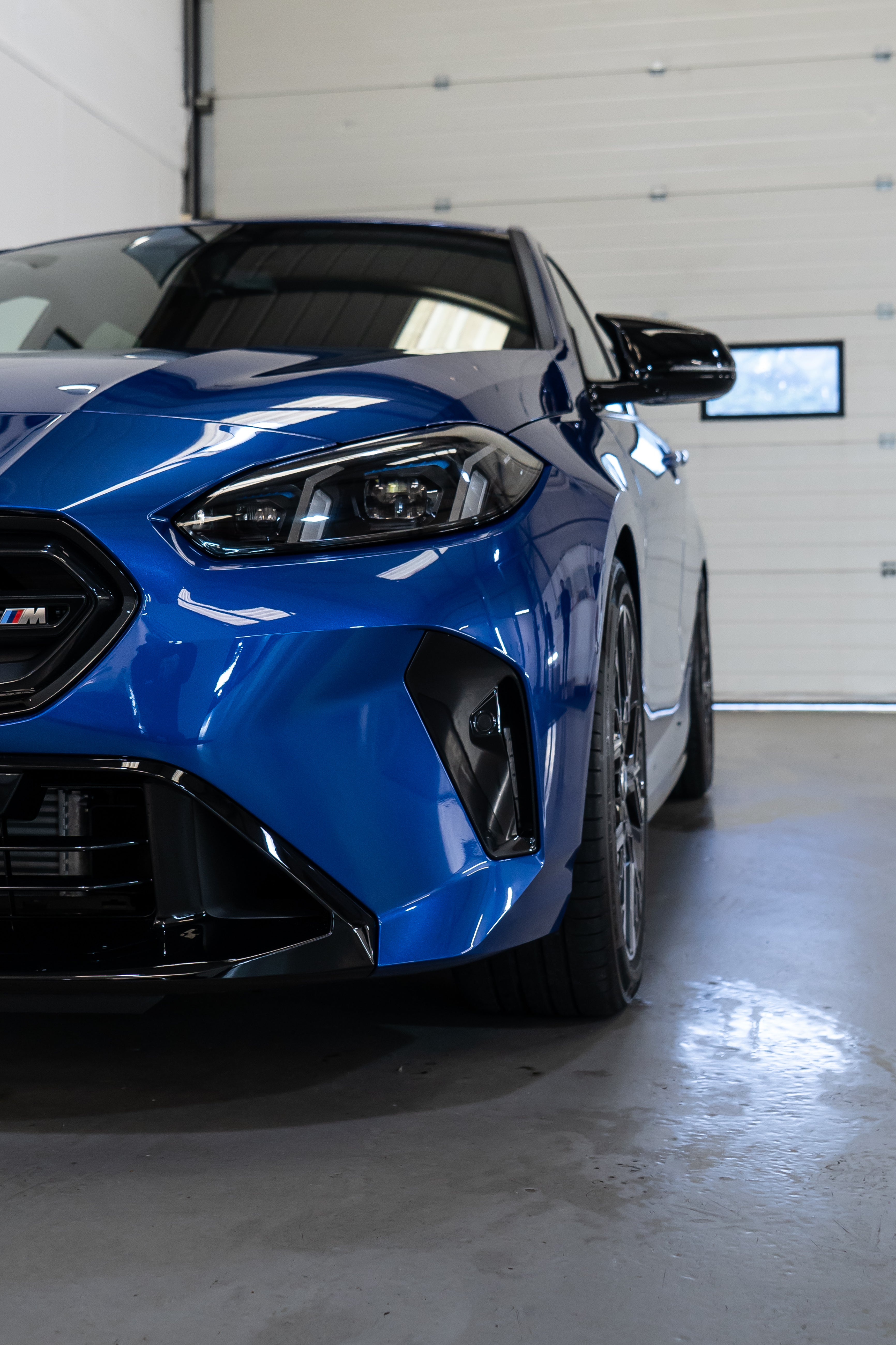 Front of a Blue BMW F70 with Motech stance springs parked in a workshop. 