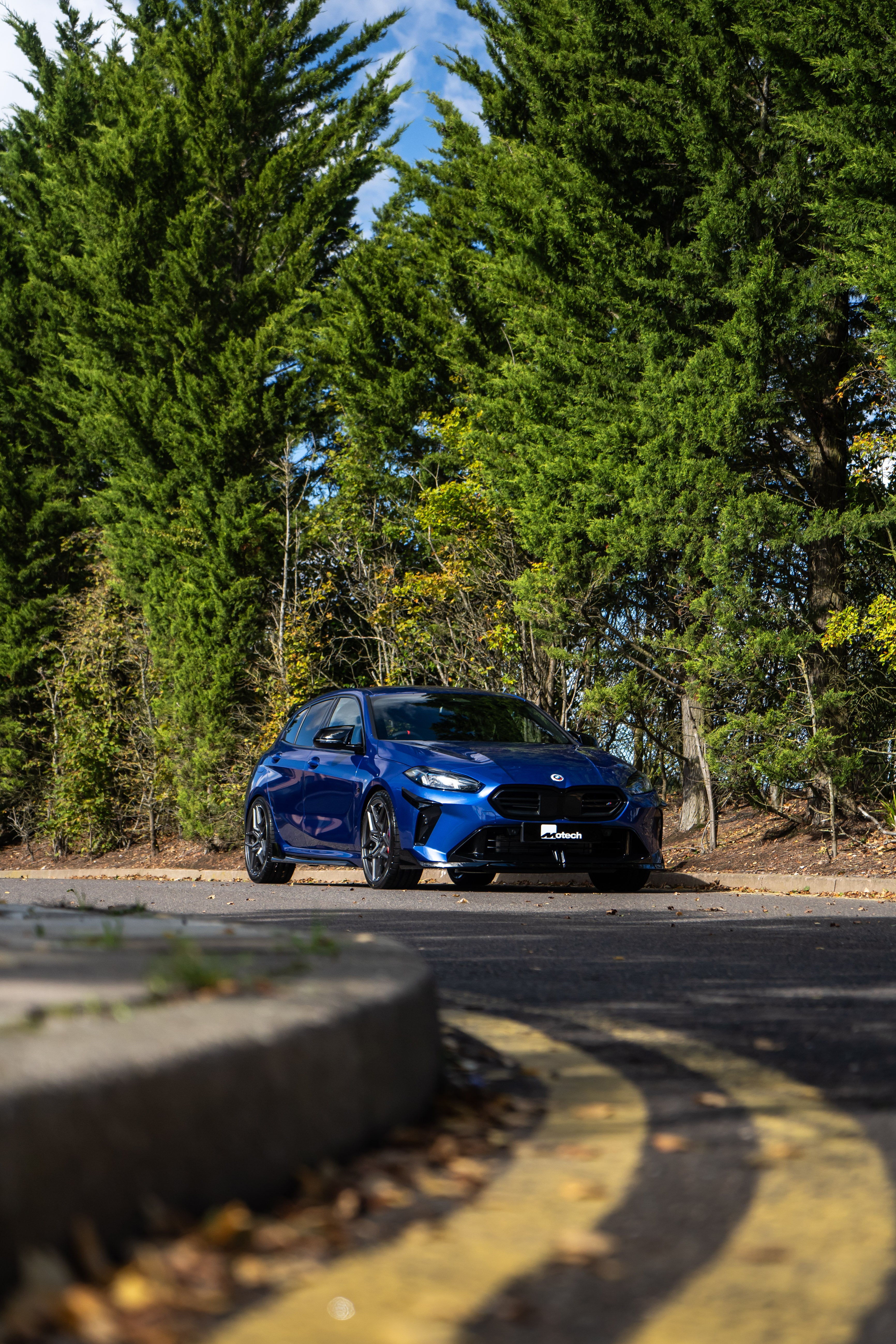 Front of a Blue BMW F70 with Motech stance springs parked in front of some trees.