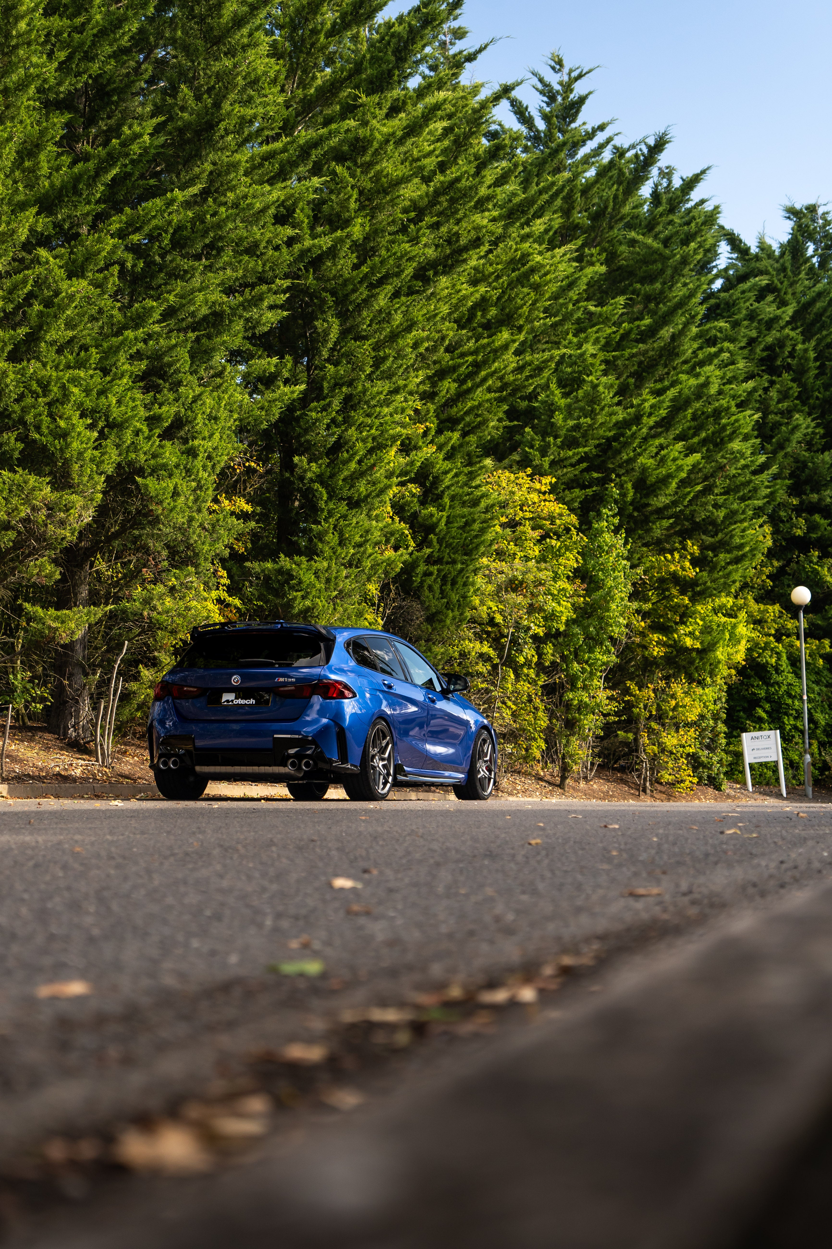 Rear of a Blue BMW F70 with Motech stance springs parked in front of some trees.