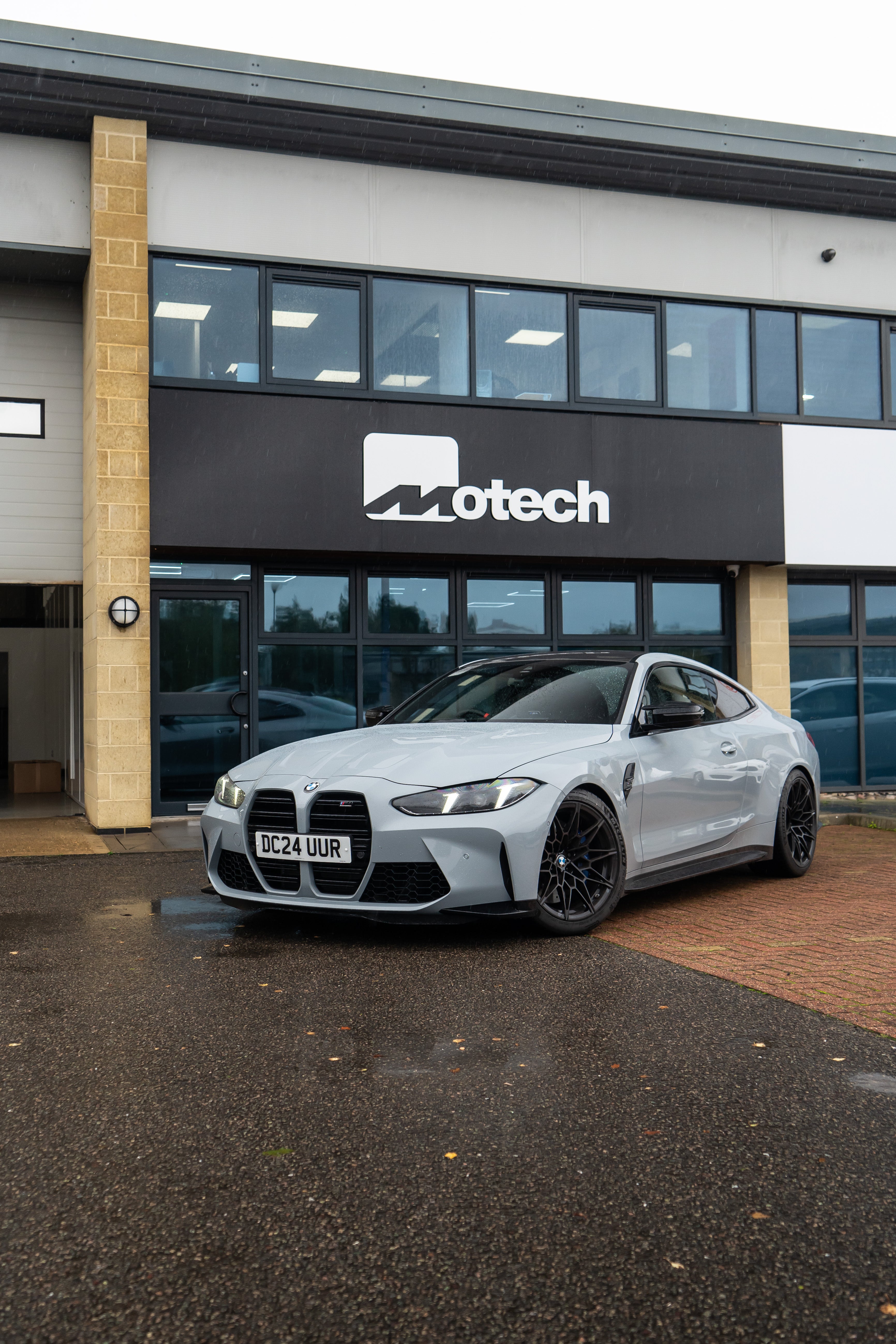 Grey BMW M4 on Motech stance springs parked outside a building with 'Motech' branding. 