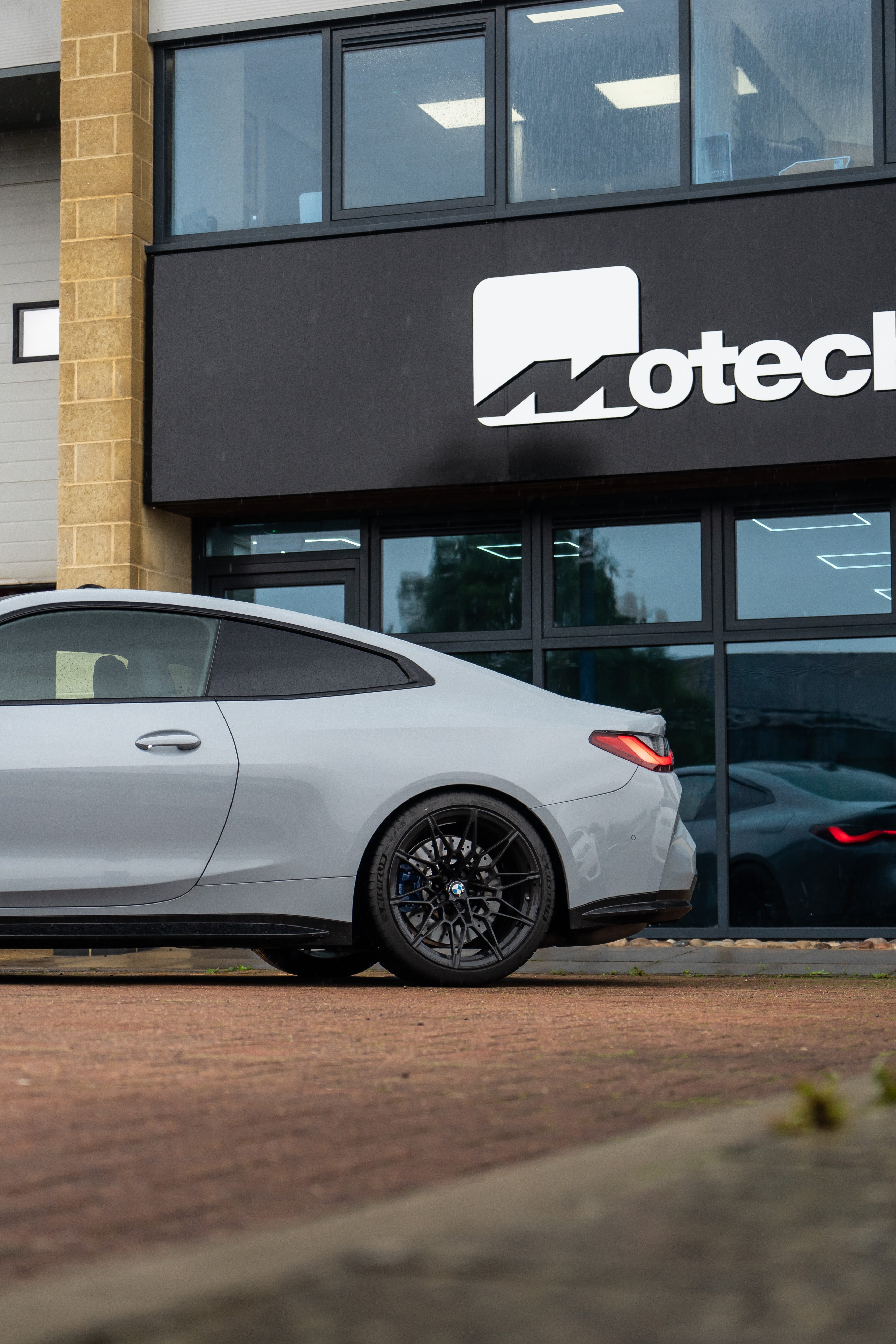 Rear of a Grey BMW M4 on Motech stance springs parked outside a building with 'Motech' branding. 