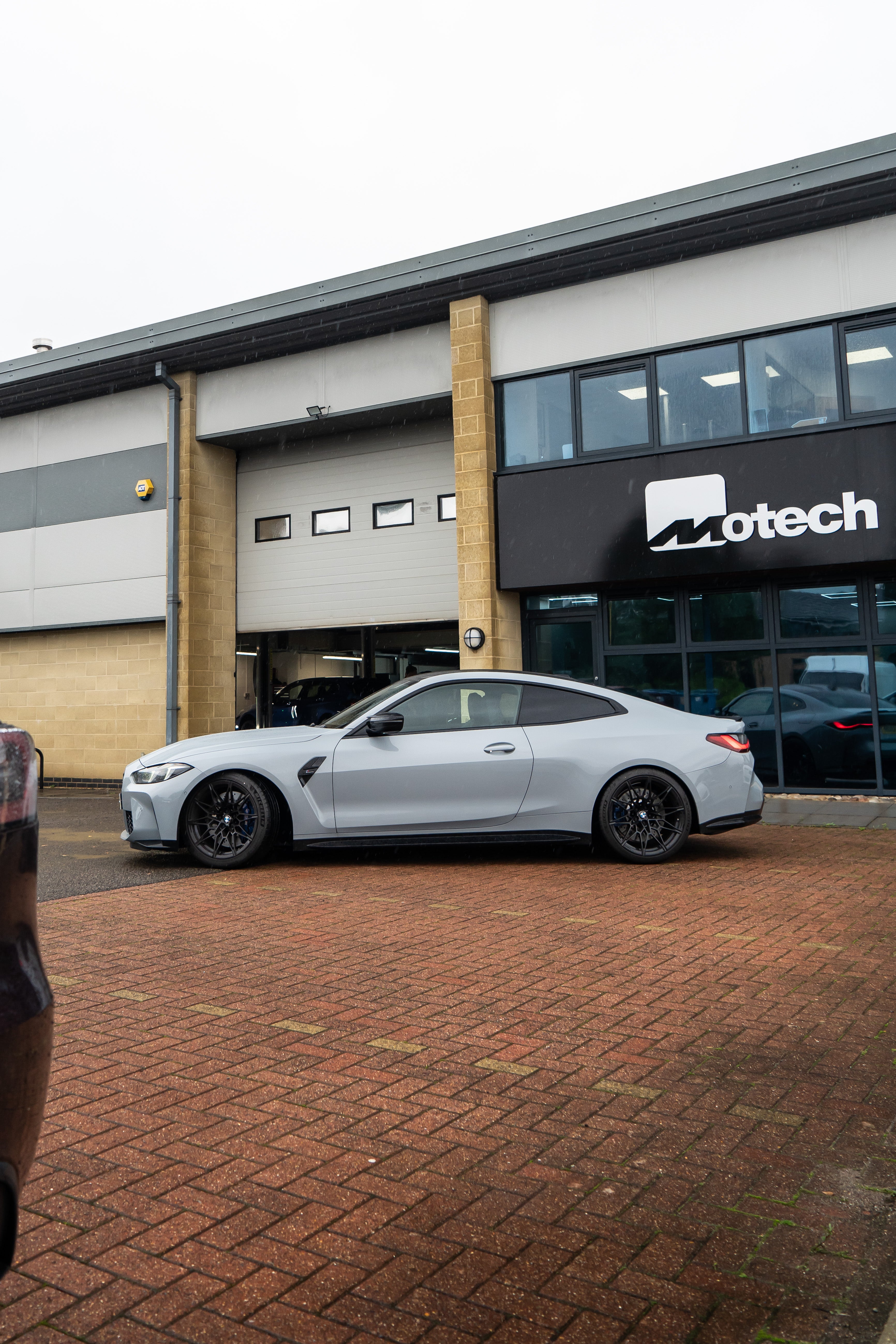 Side-on shot of a Grey BMW M4 on Motech stance springs parked outside a building with 'Motech' branding. 