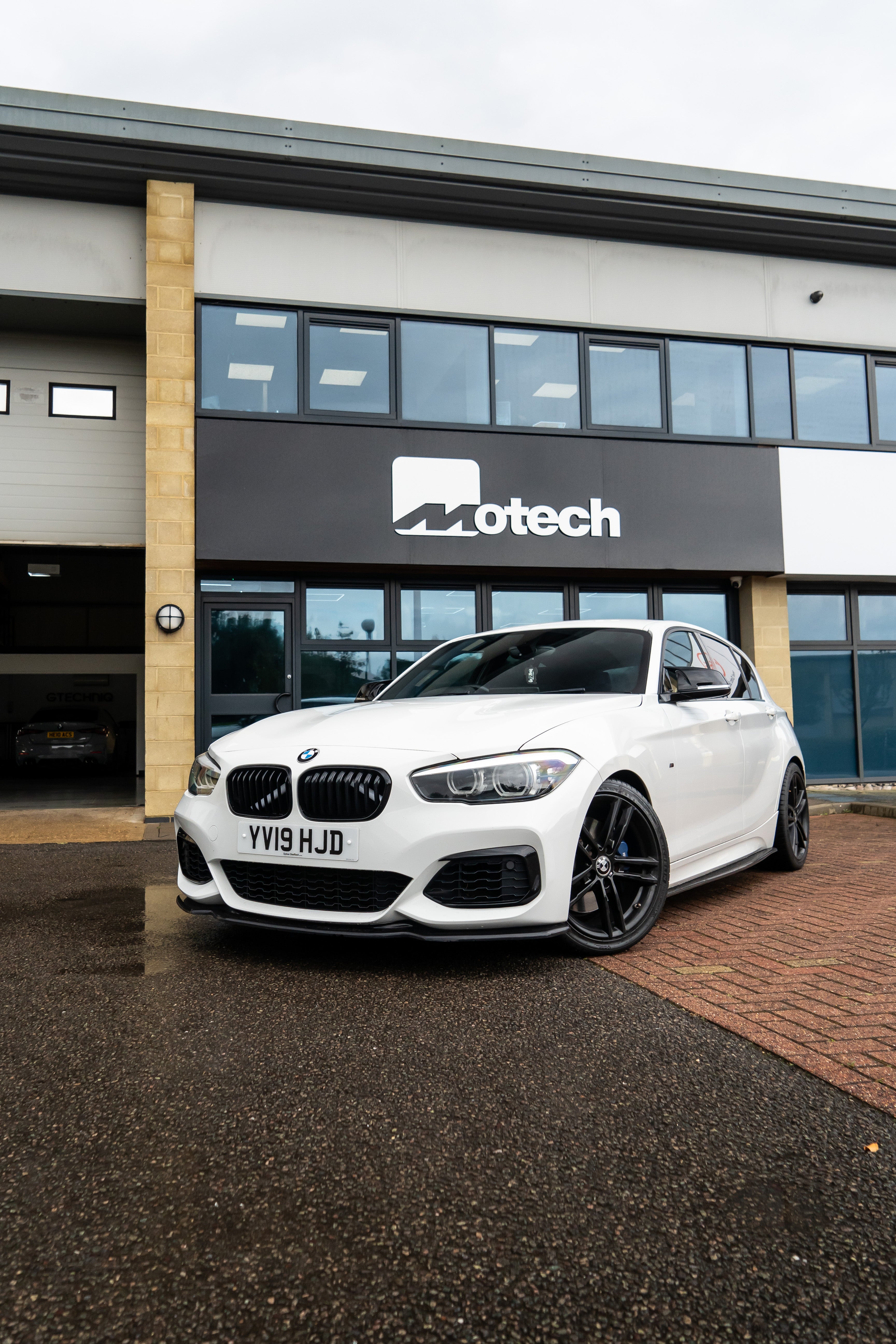 White BMW 1 Series on Motech stance springs parked outside a building with 'Motech' branding.