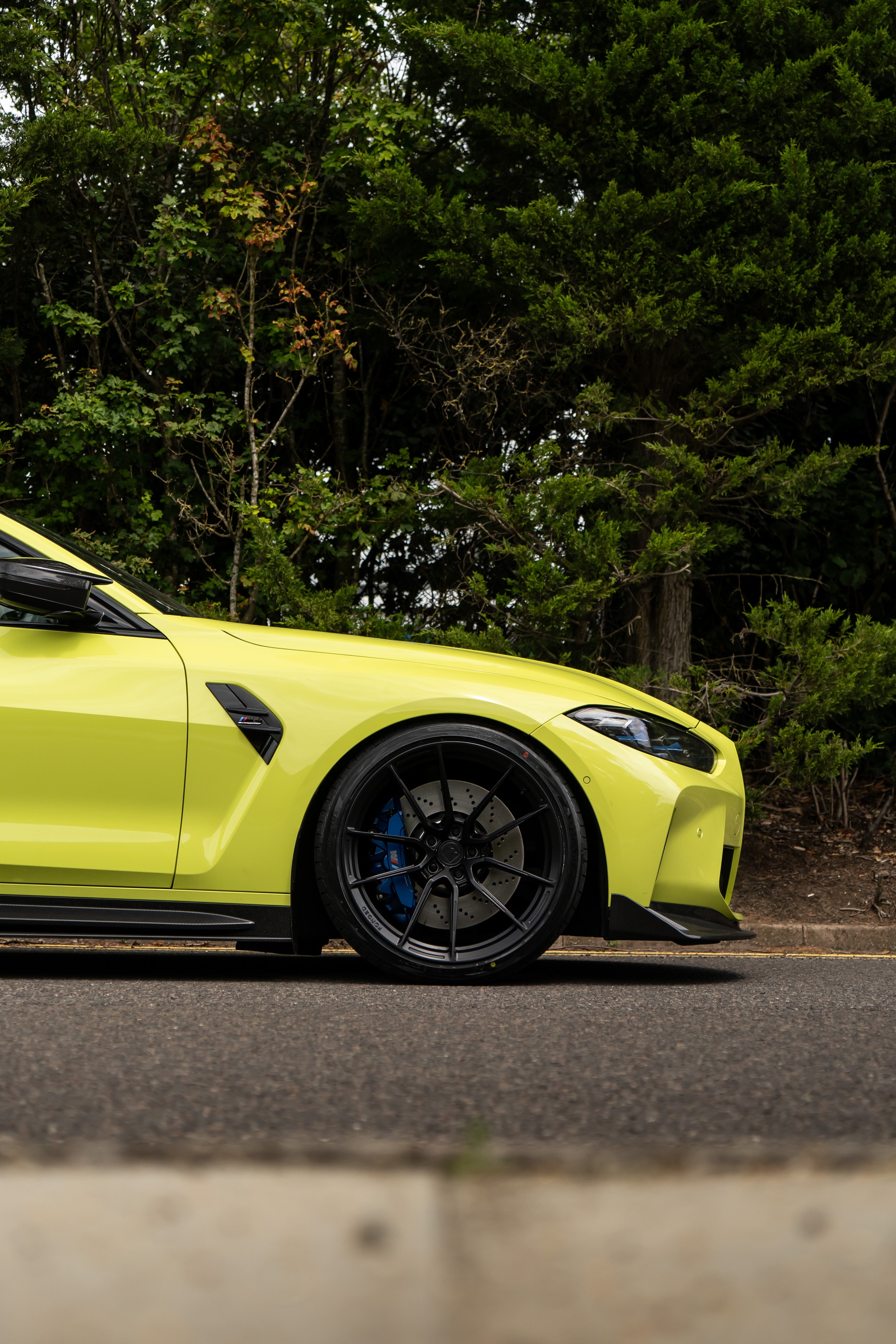 Front of a São Paulo Yellow BMW M4 on Motech Stance Springs parked in front of some trees. 
