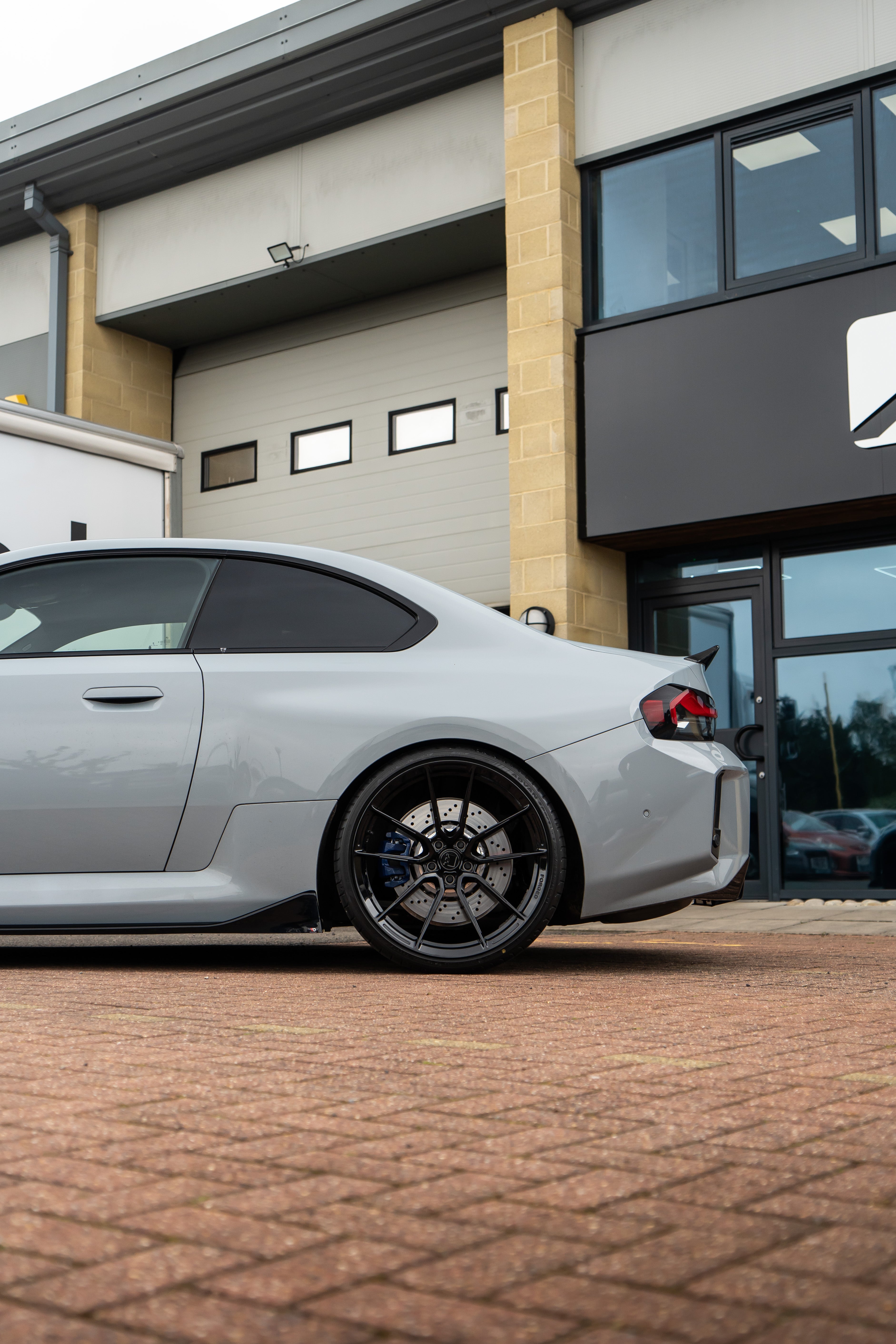 Rear shot of a Grey BMW M2 G87 on Motech Stance Springs parked outside a building with red bricks on the floor. 