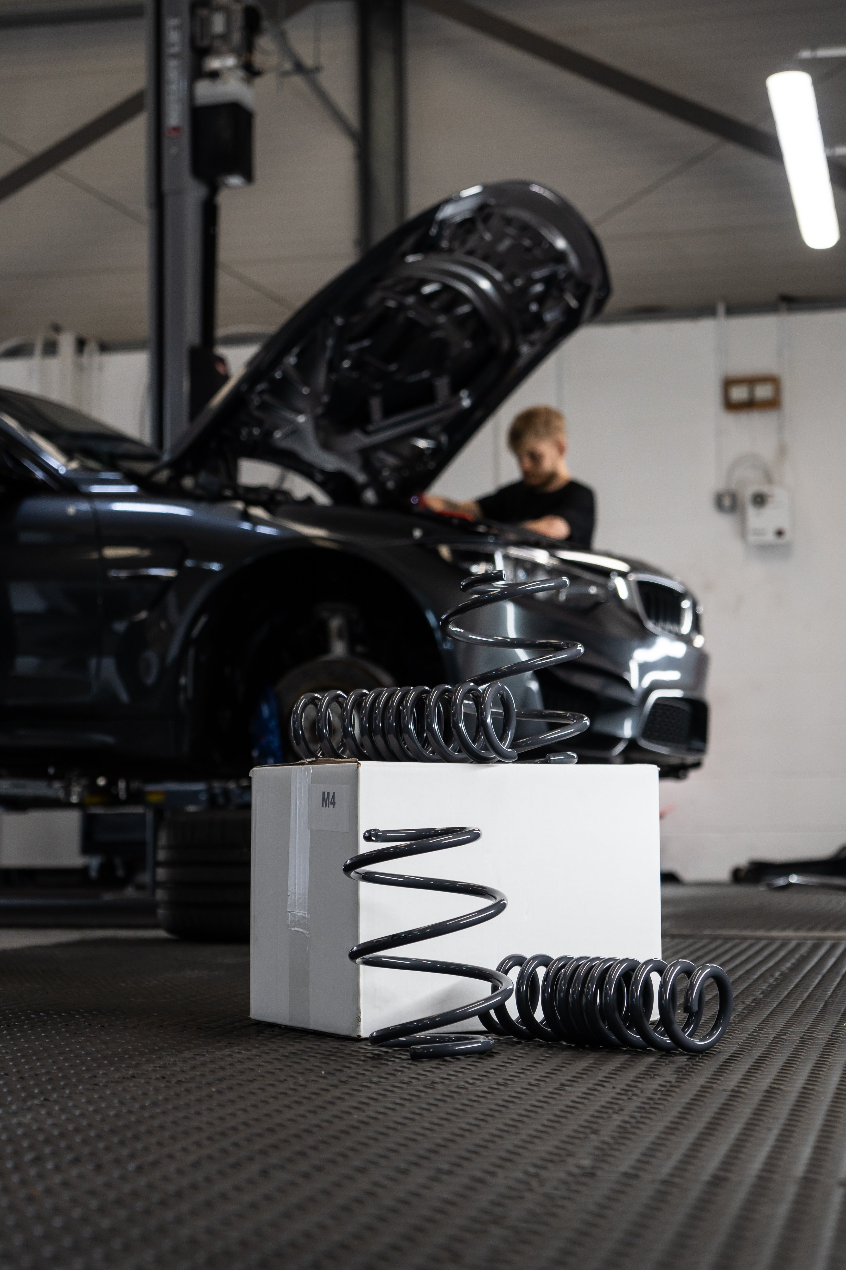Lowering Springs on a white box with someone working on a car in the background.