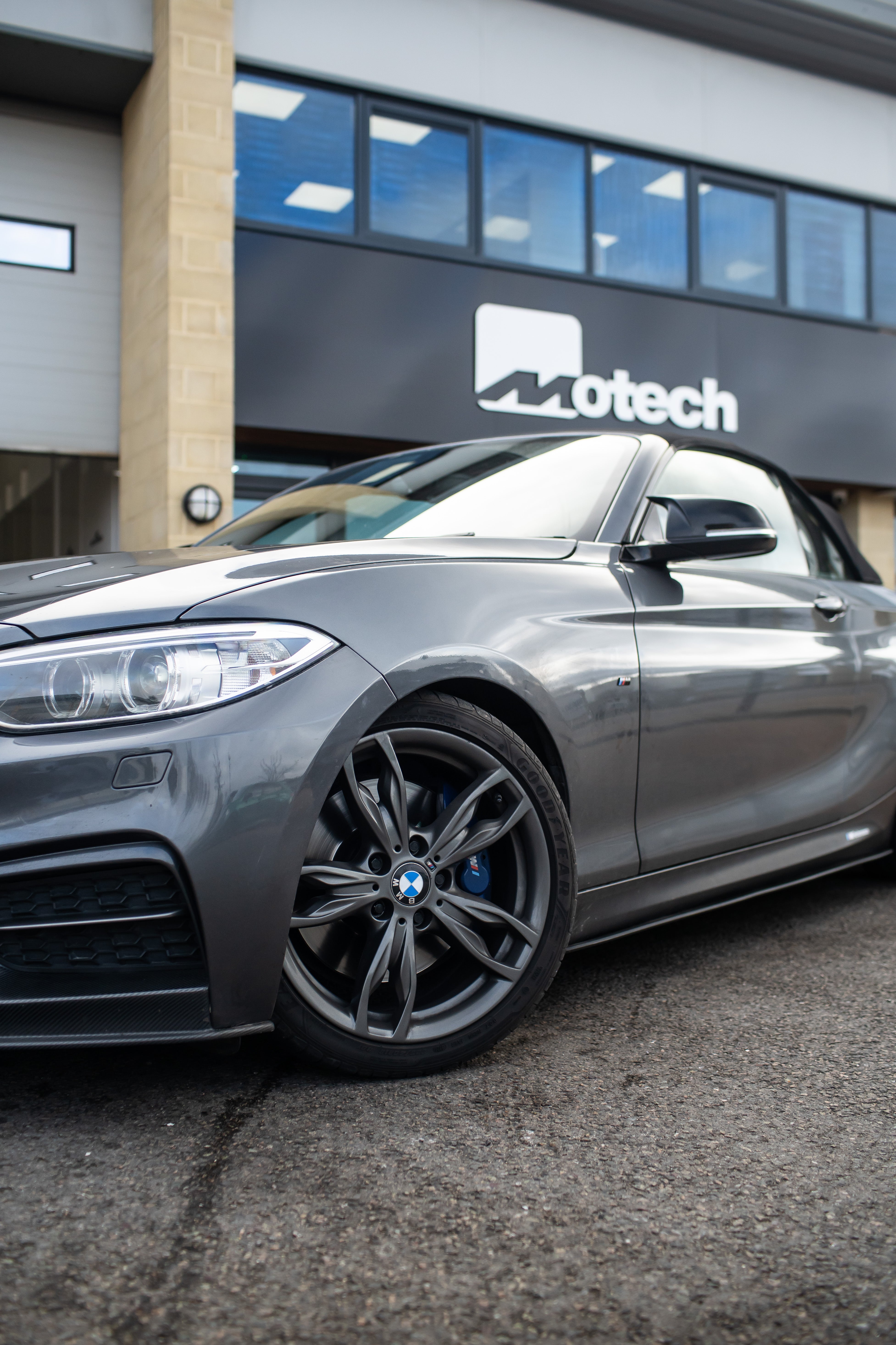 The front of a Grey BMW 2 Series on Motech Stance Springs parked outside the Motech building.