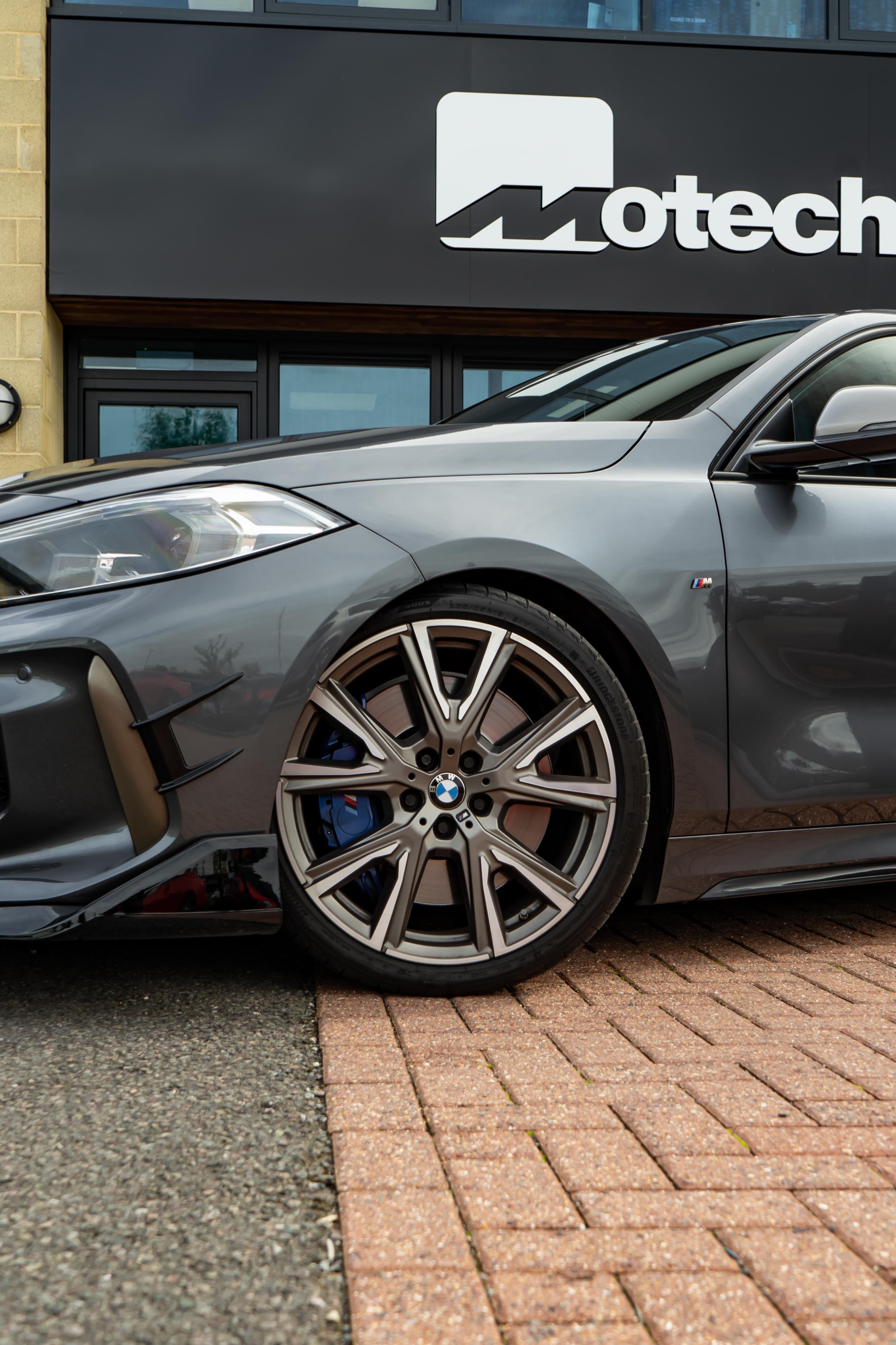 Grey BMW car parked in front of a building with 'Motech' branding.