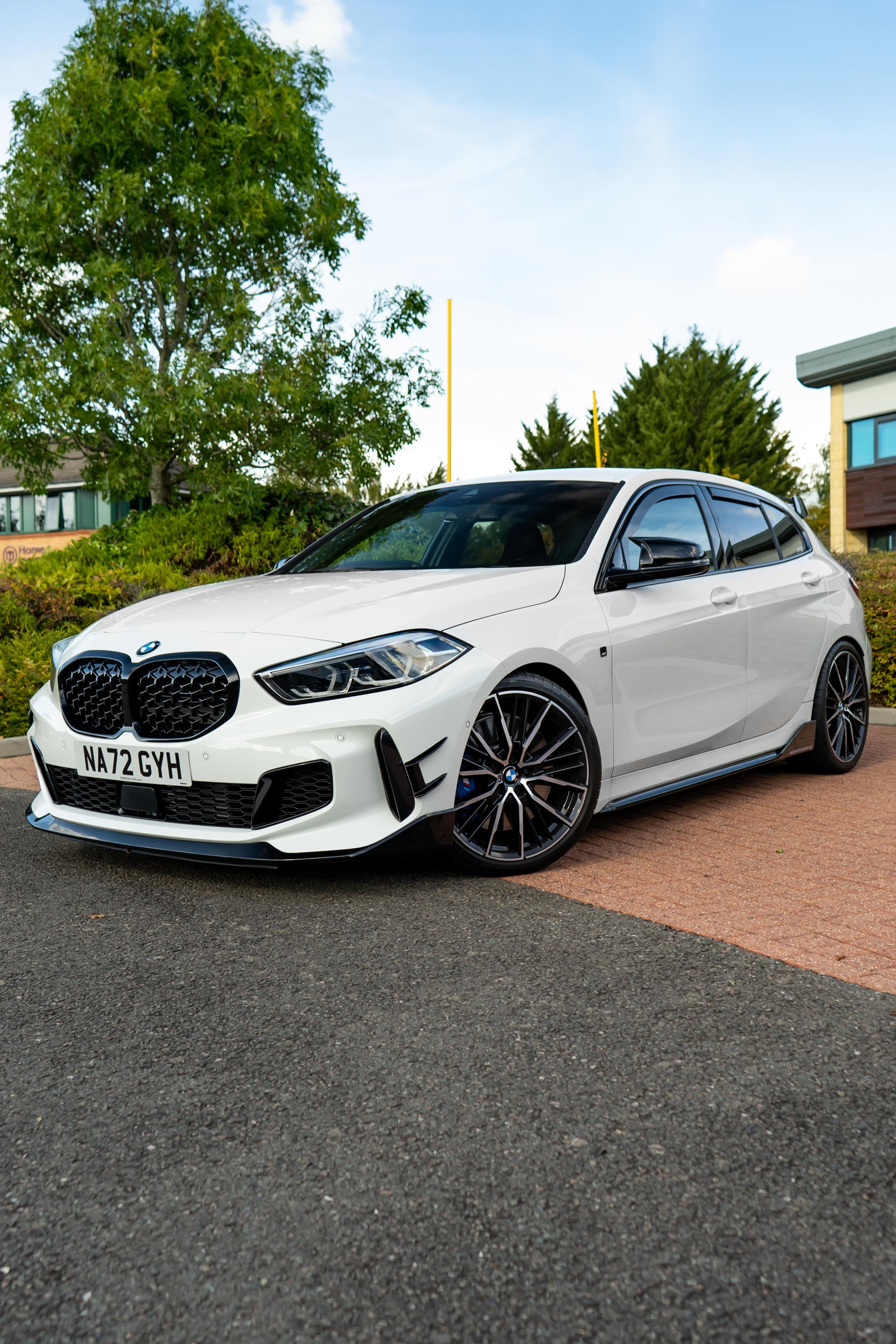 White BMW car parked on a road with trees and buildings in the background