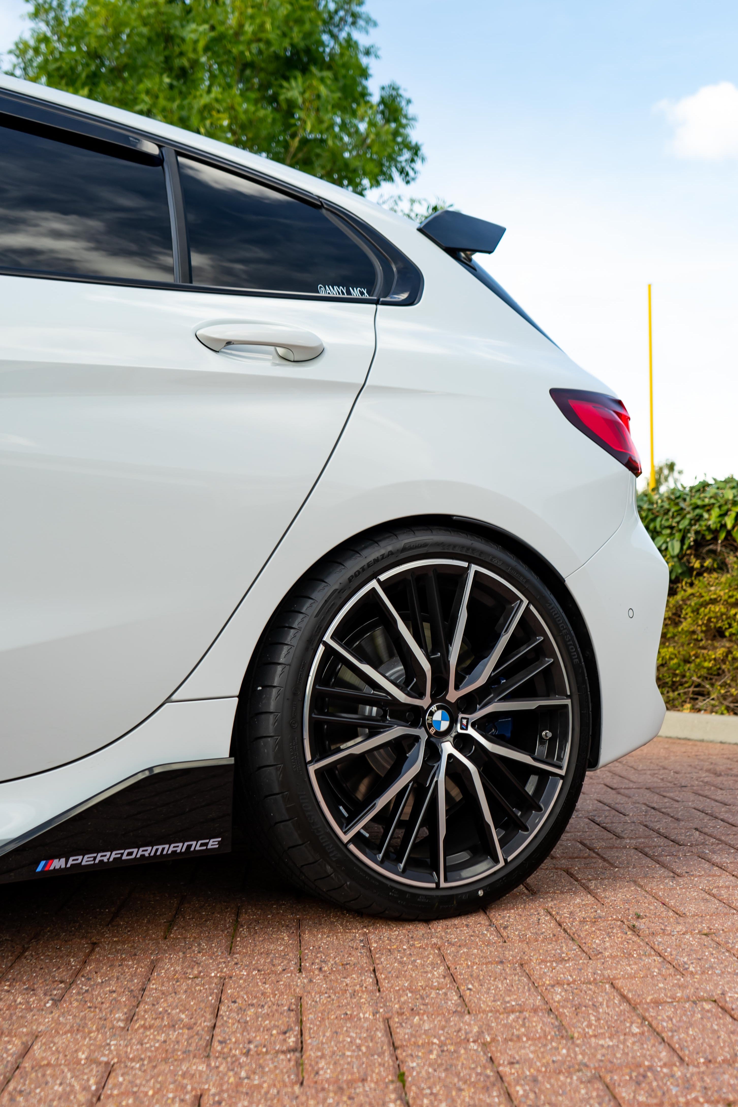 Back of a white BMW with trees and bushes in the background