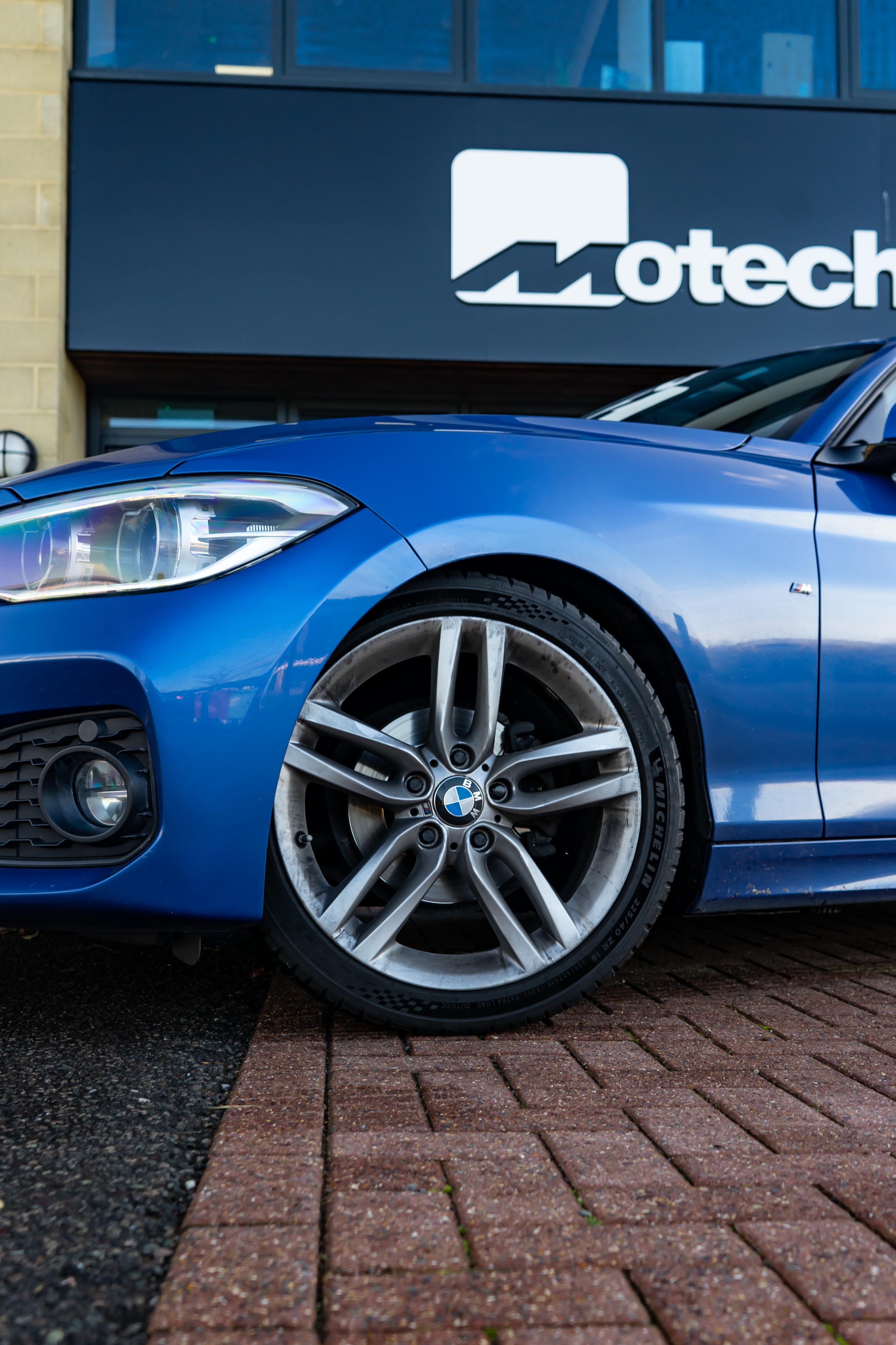 Front of a Blue BMW on Motech Stance Springs parked outside a building with 'Motech' branding. 