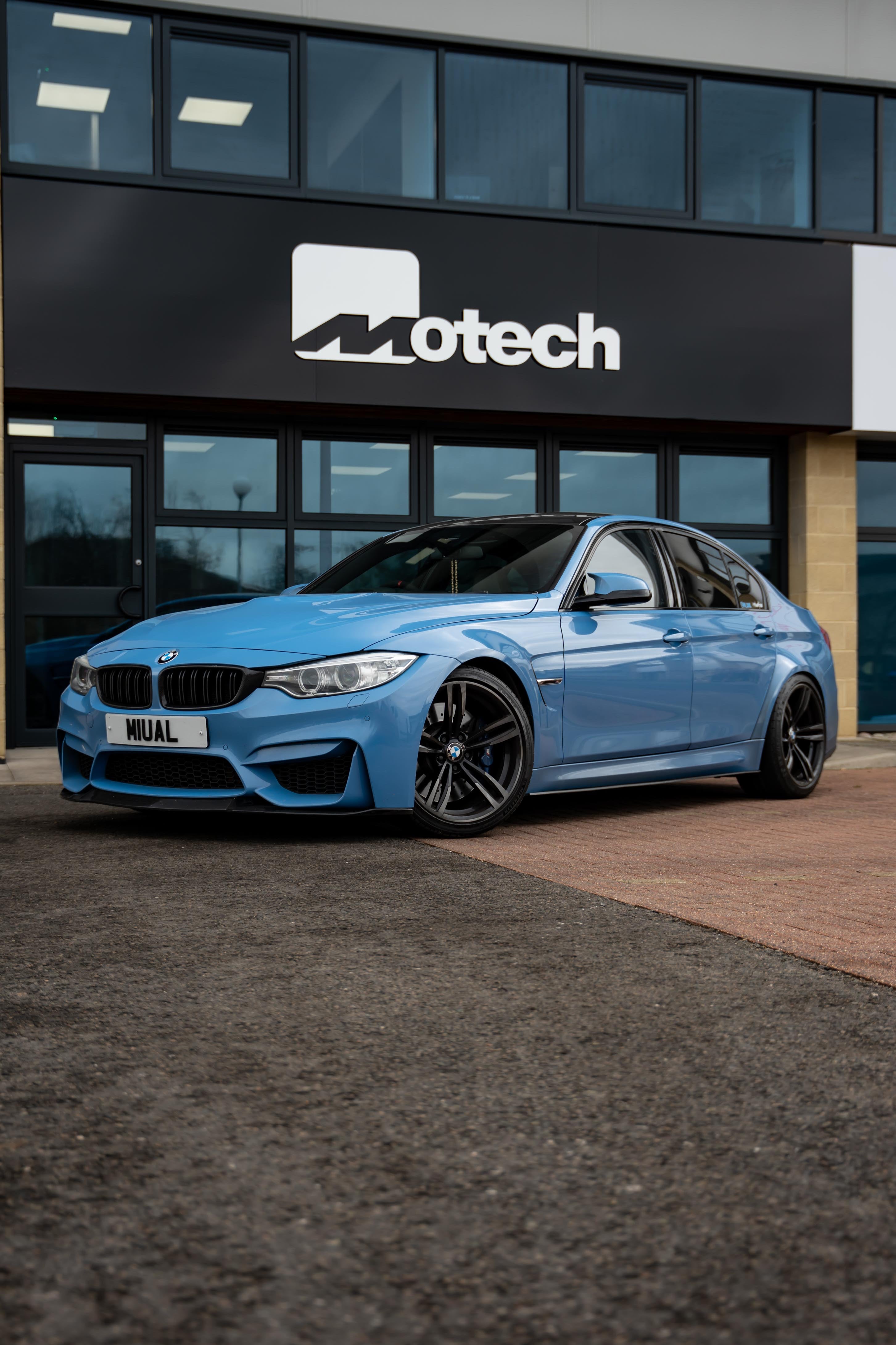 Blue BMW car parked in front of a building with 'Motech' branding.