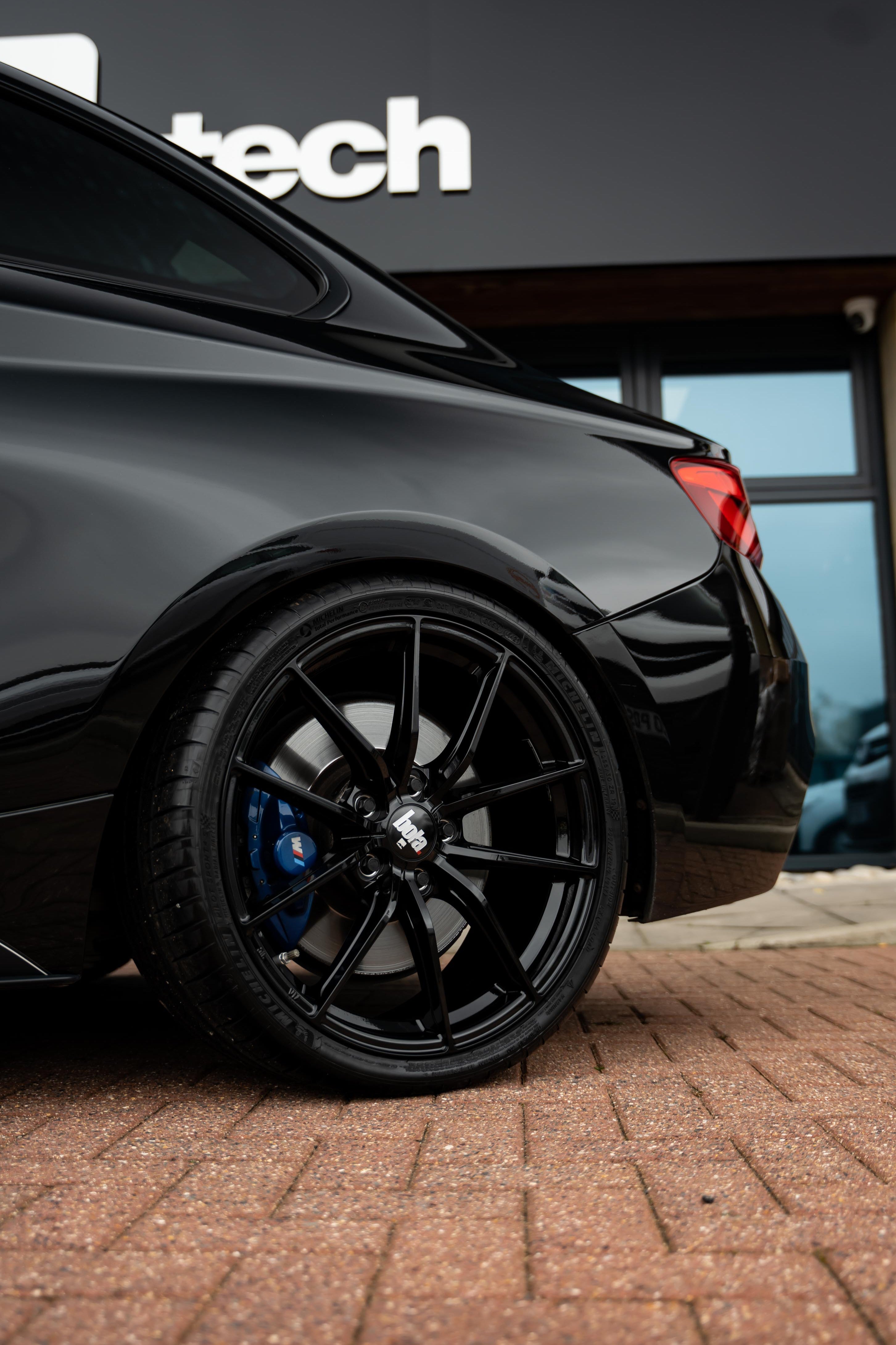 Black BMW with black 'Bola' branded wheels parked in front of a building with 'Motech' branding.