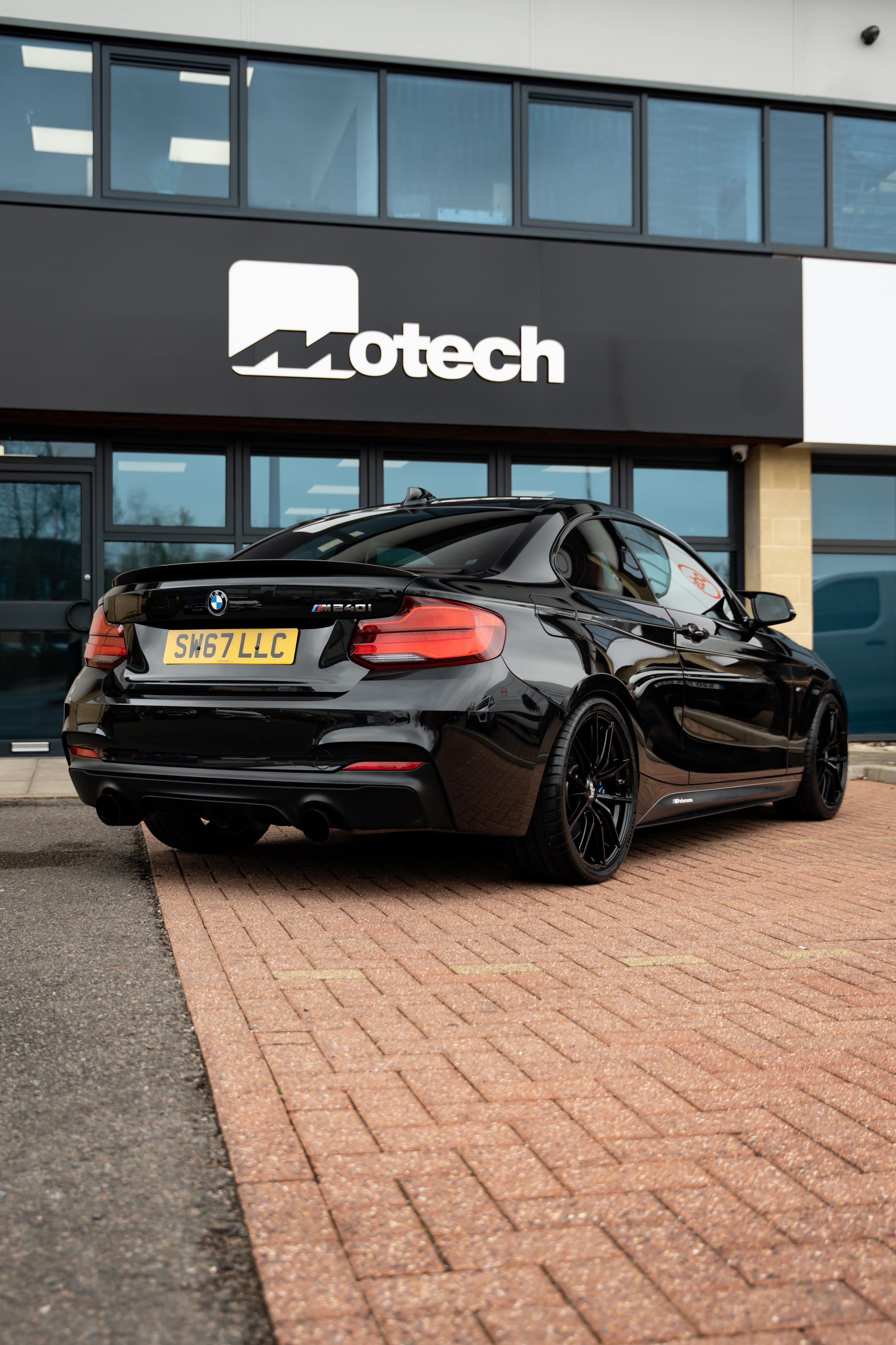 Black BMW car on Motech Stance springs parked in front of a building with 'Motech' branding.